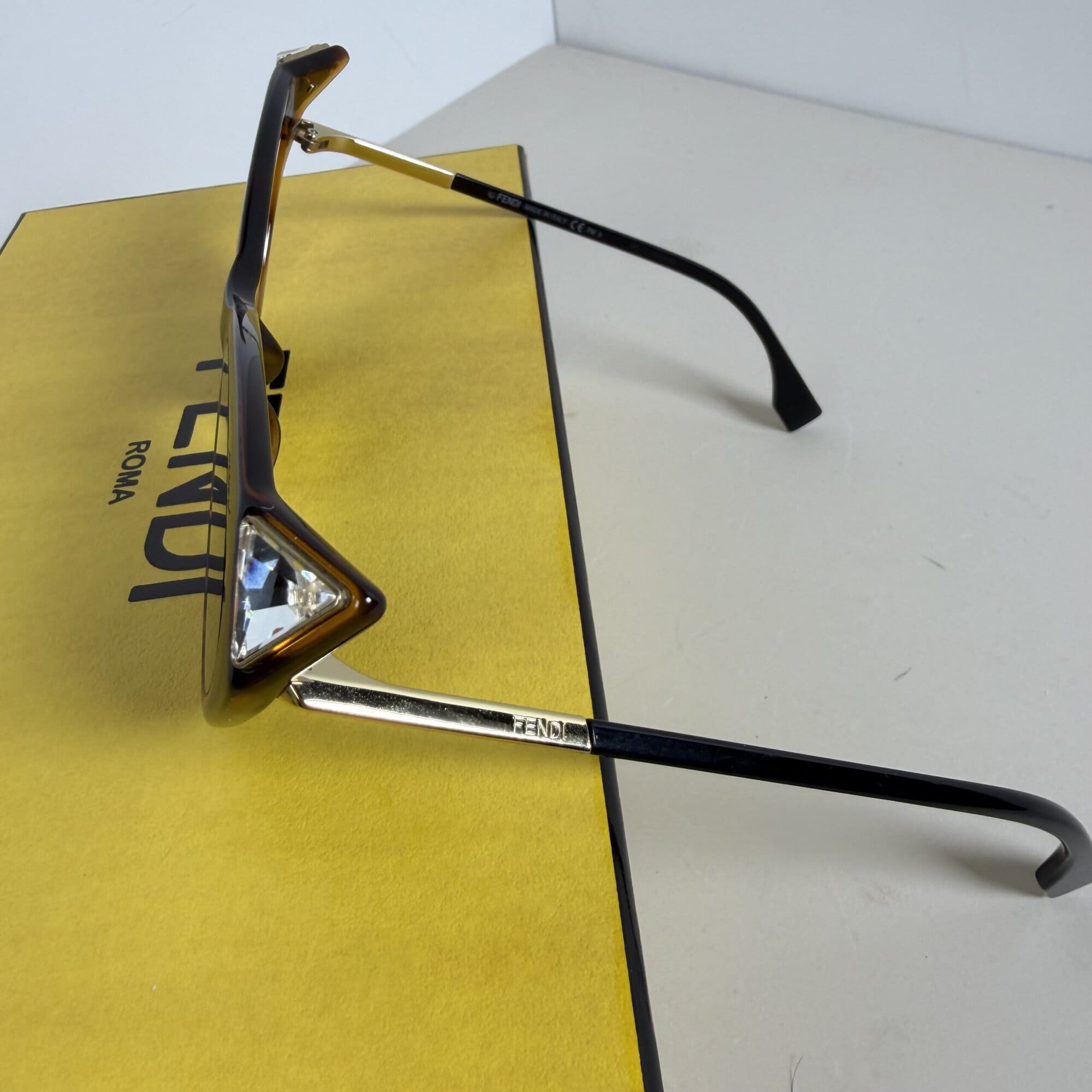 Side angle of Fendi sunglasses showing gold-tone temple arm with engraved logo and faceted corner stud