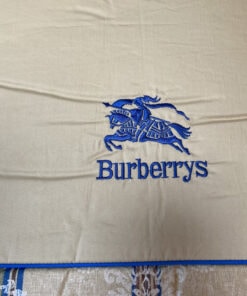 Royal blue embroidered Burberrys Equestrian Knight logo and lettering on beige fabric.