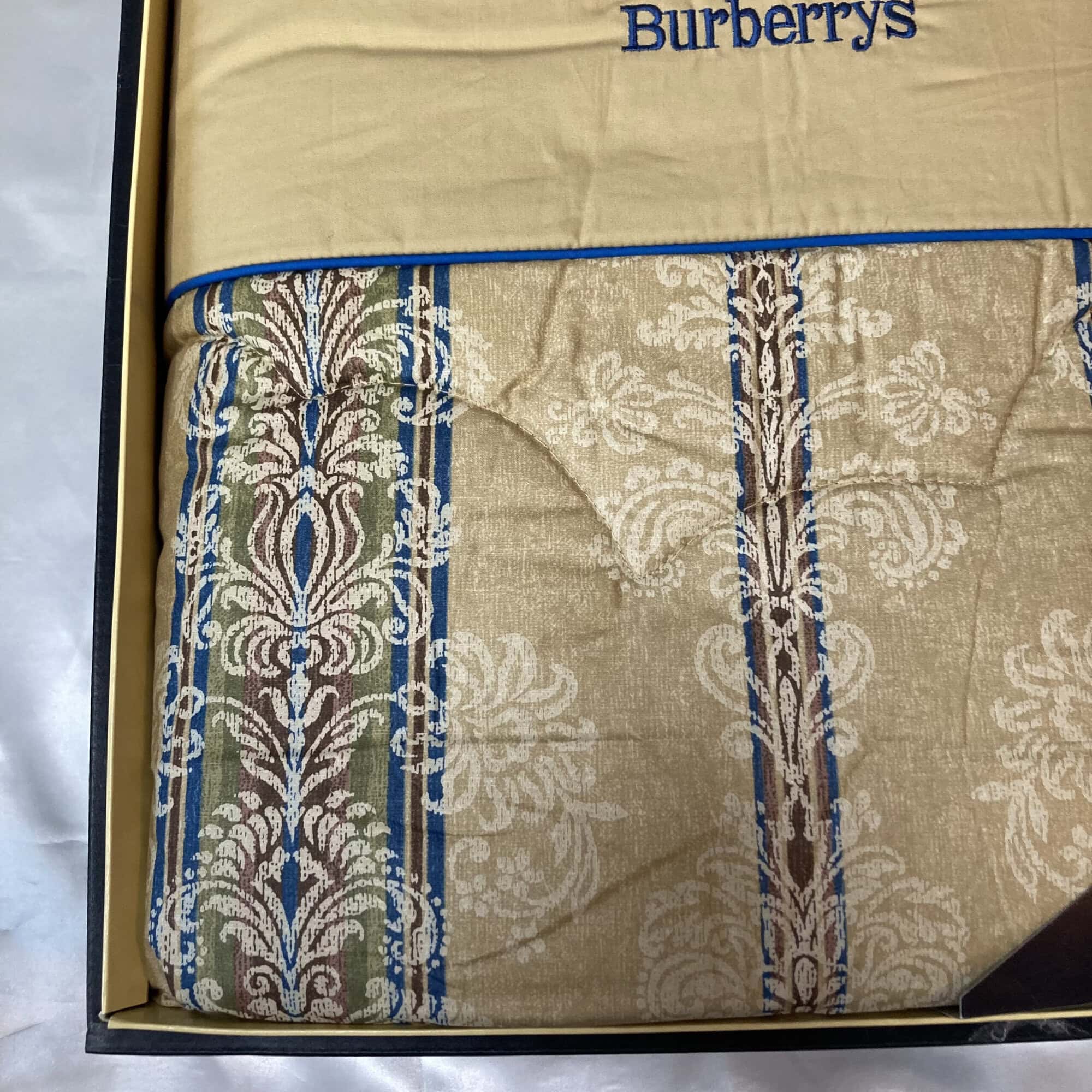 Close-up of the beige and blue damask jacquard textile weave with quilted stitching.