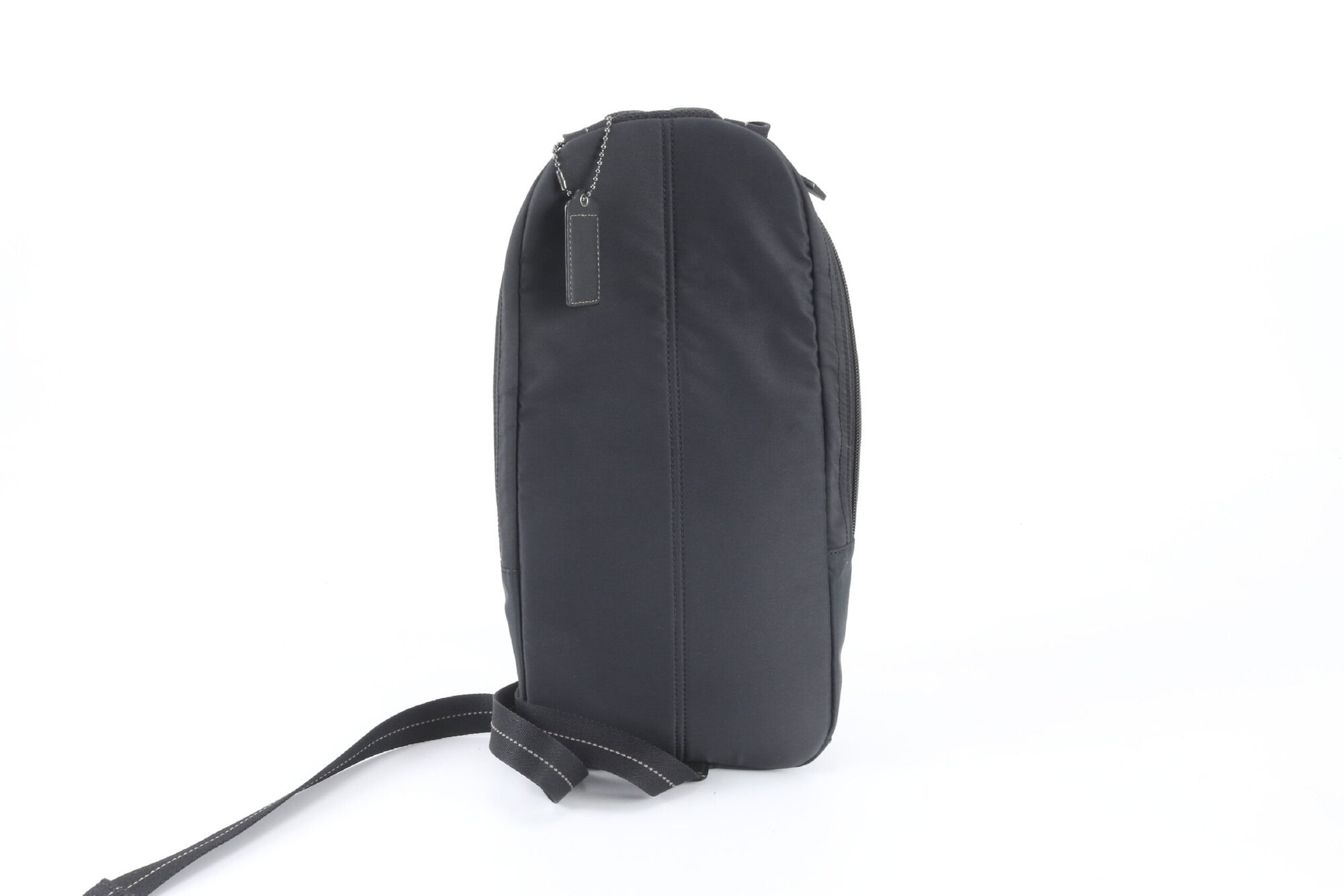 Rear view of Coach black sling pack showing back panel and hangtag
