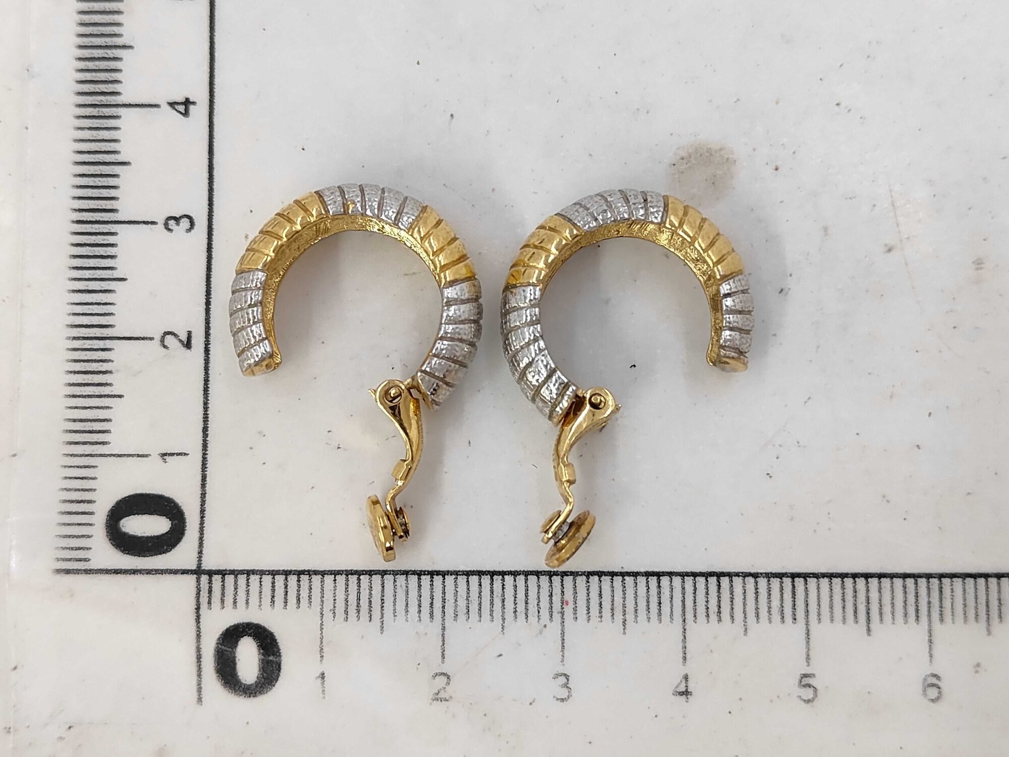 Givenchy two-tone ribbed hoop clip-on earrings positioned next to a metric measuring ruler.