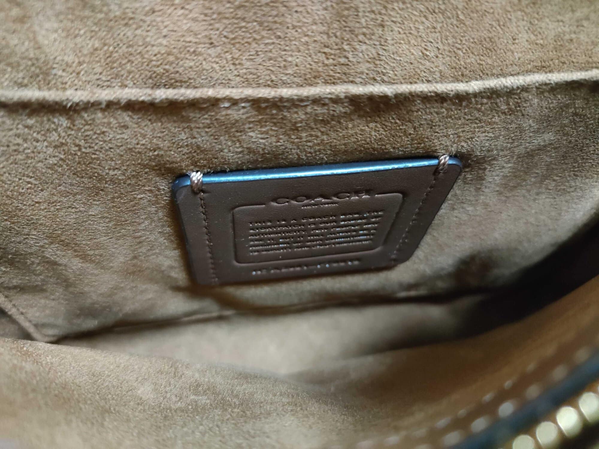 Close-up of stitched leather Coach creed patch on interior pocket wall