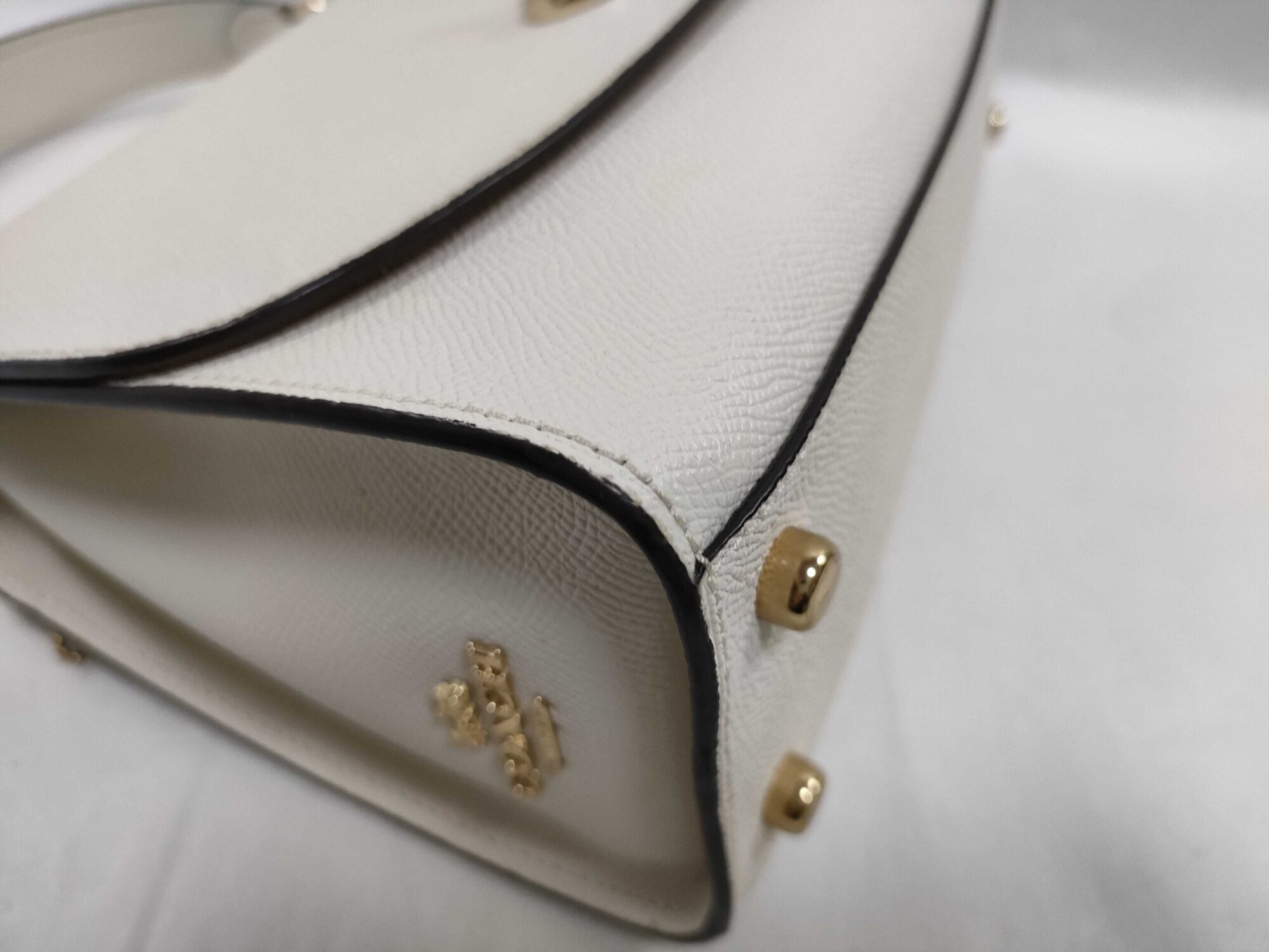 Side gusset and corner view of Coach satchel showing edge glazing and gold-tone base studs