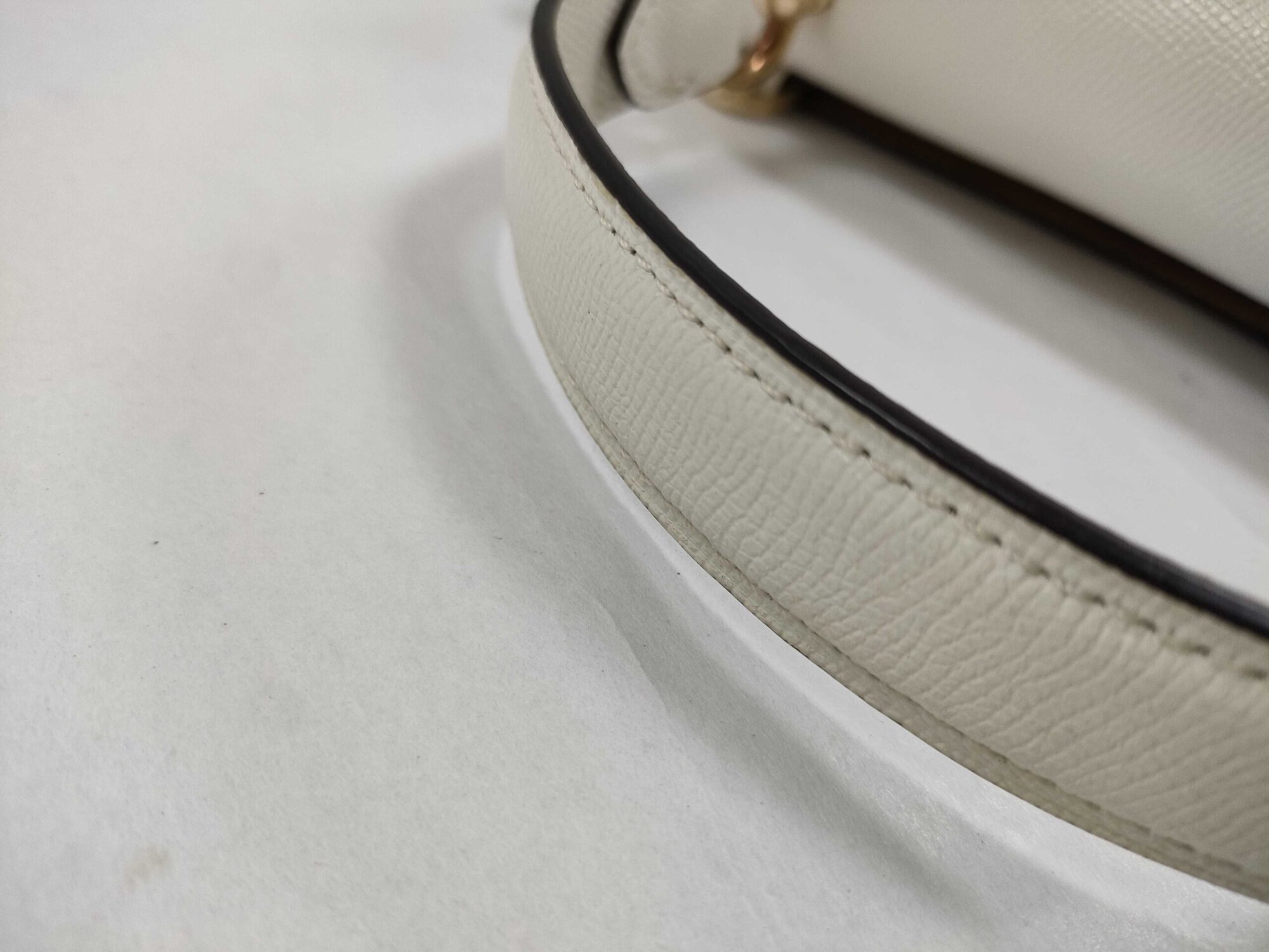 Detail of white crossgrain leather texture and edge stitching on satchel top handle