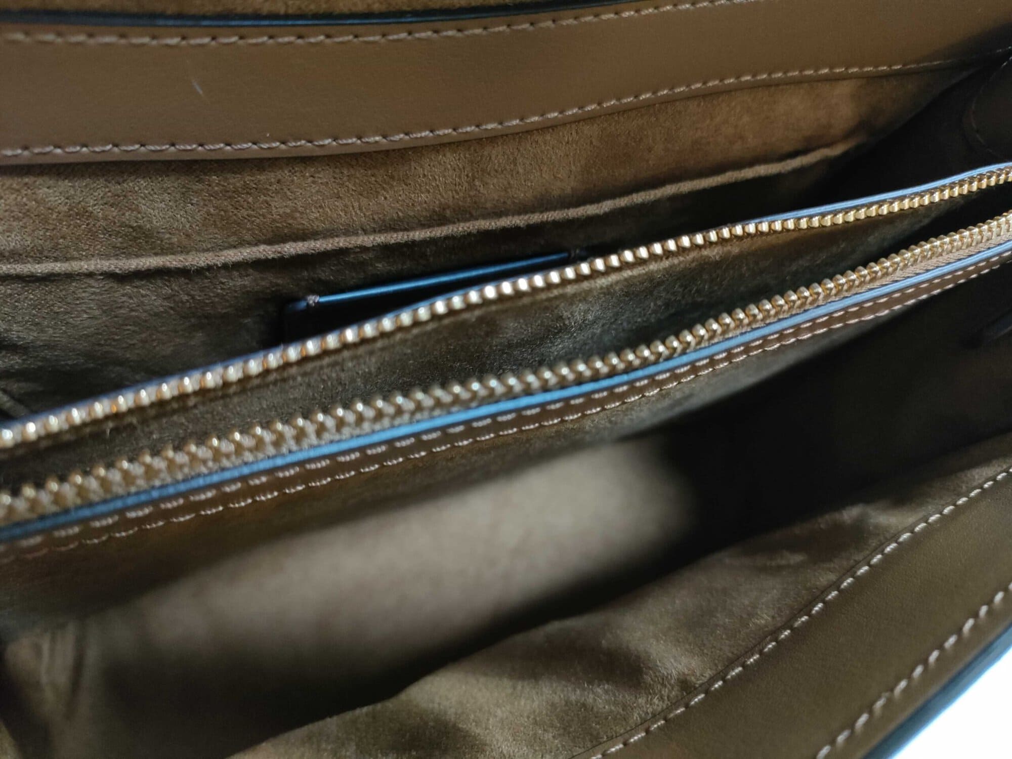 Interior compartment of Coach satchel showing tan textile lining and gold-tone zip wall pocket