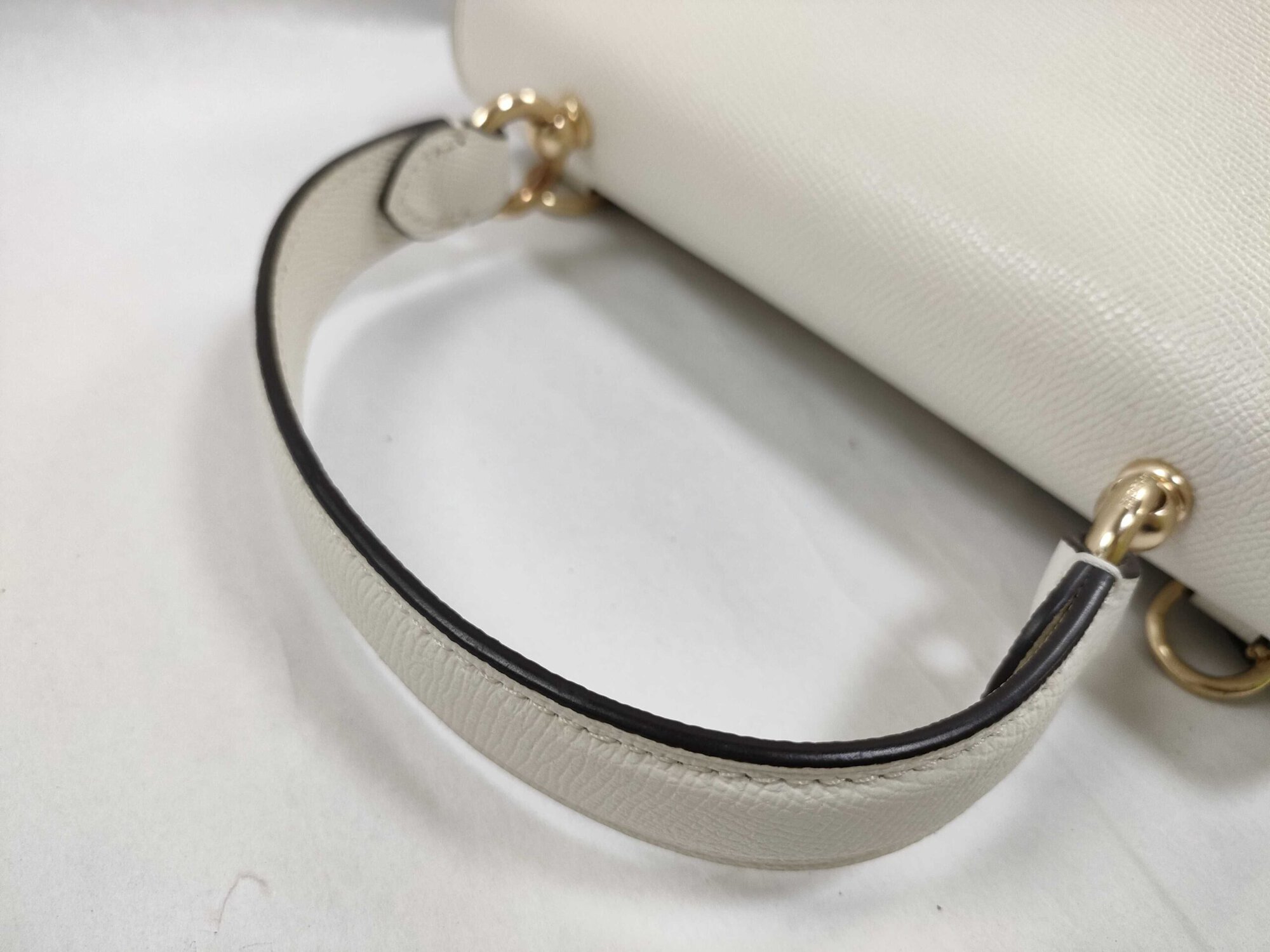Close-up of rolled leather top handle and gold-tone anchor hardware on Coach satchel