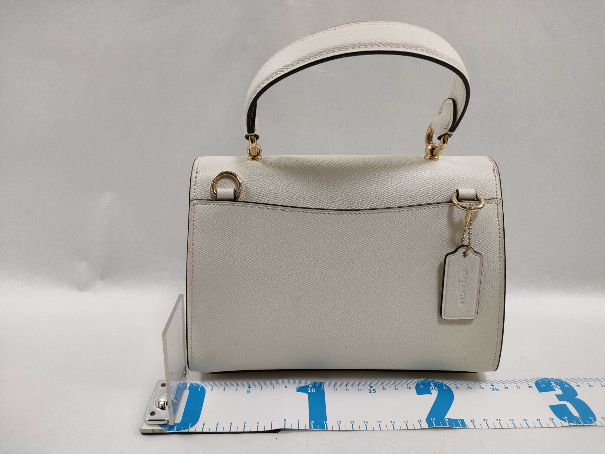 Back view of Coach Tilly satchel showing rear slip pocket, hangtag, D-rings, and measuring tape at base