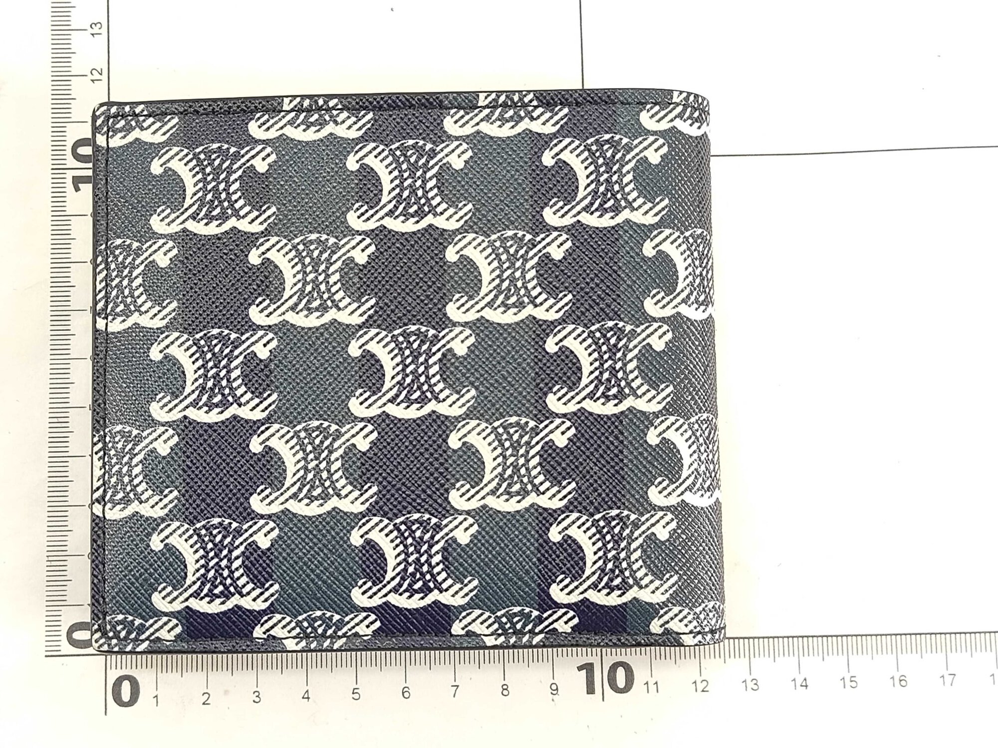Celine black Triomphe canvas bifold wallet measured flat against a metric grid ruler.