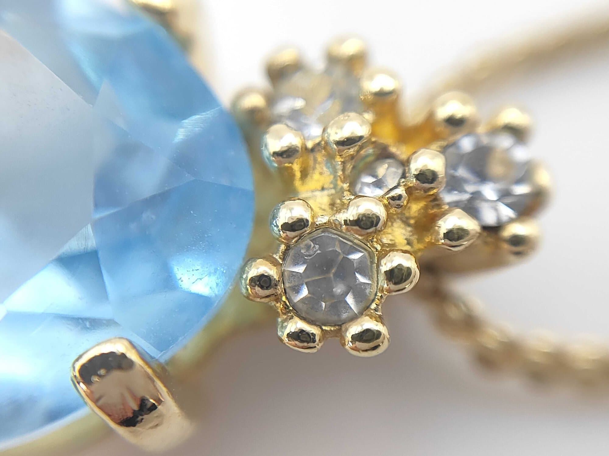 Detailed view of the three clear accent stones set in the decorative crown bail above the blue stone.