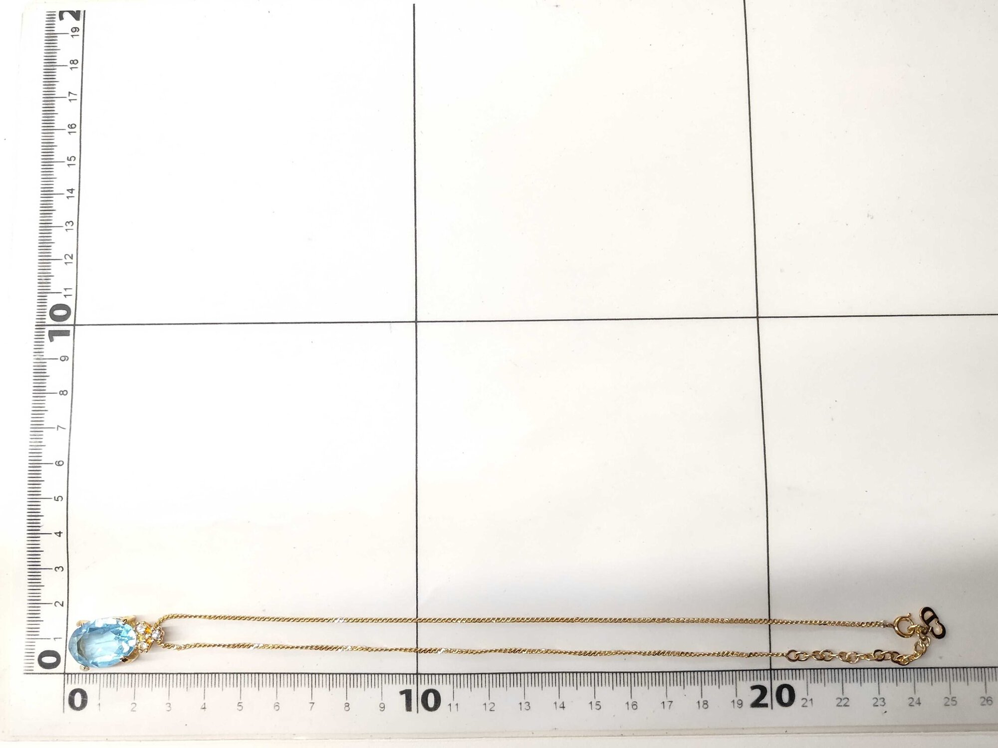 Christian Dior pendant necklace laid folded along a metric grid measuring board.