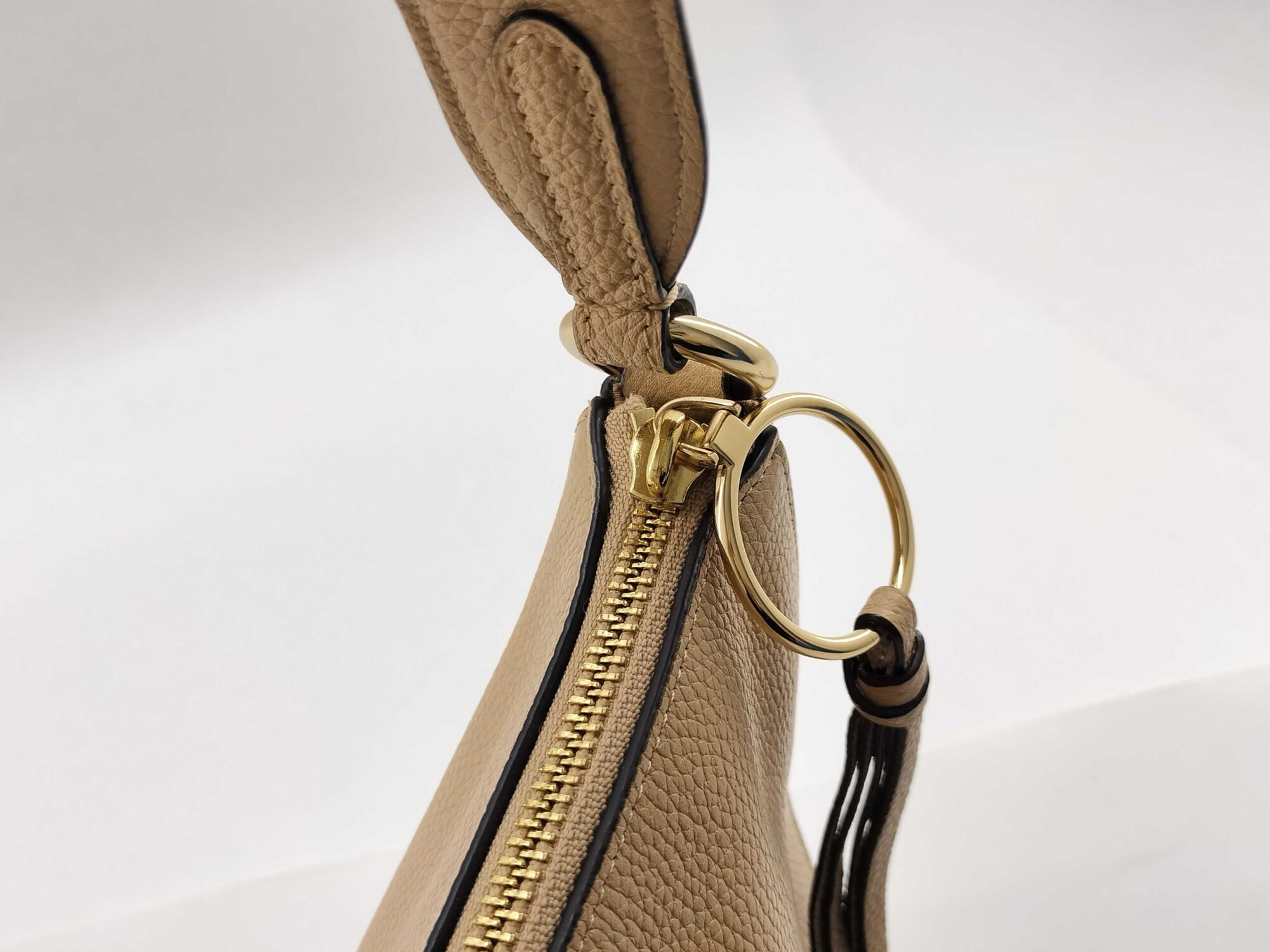 Close-up of gold-tone zipper slider with ring attachment and leather tassel pull