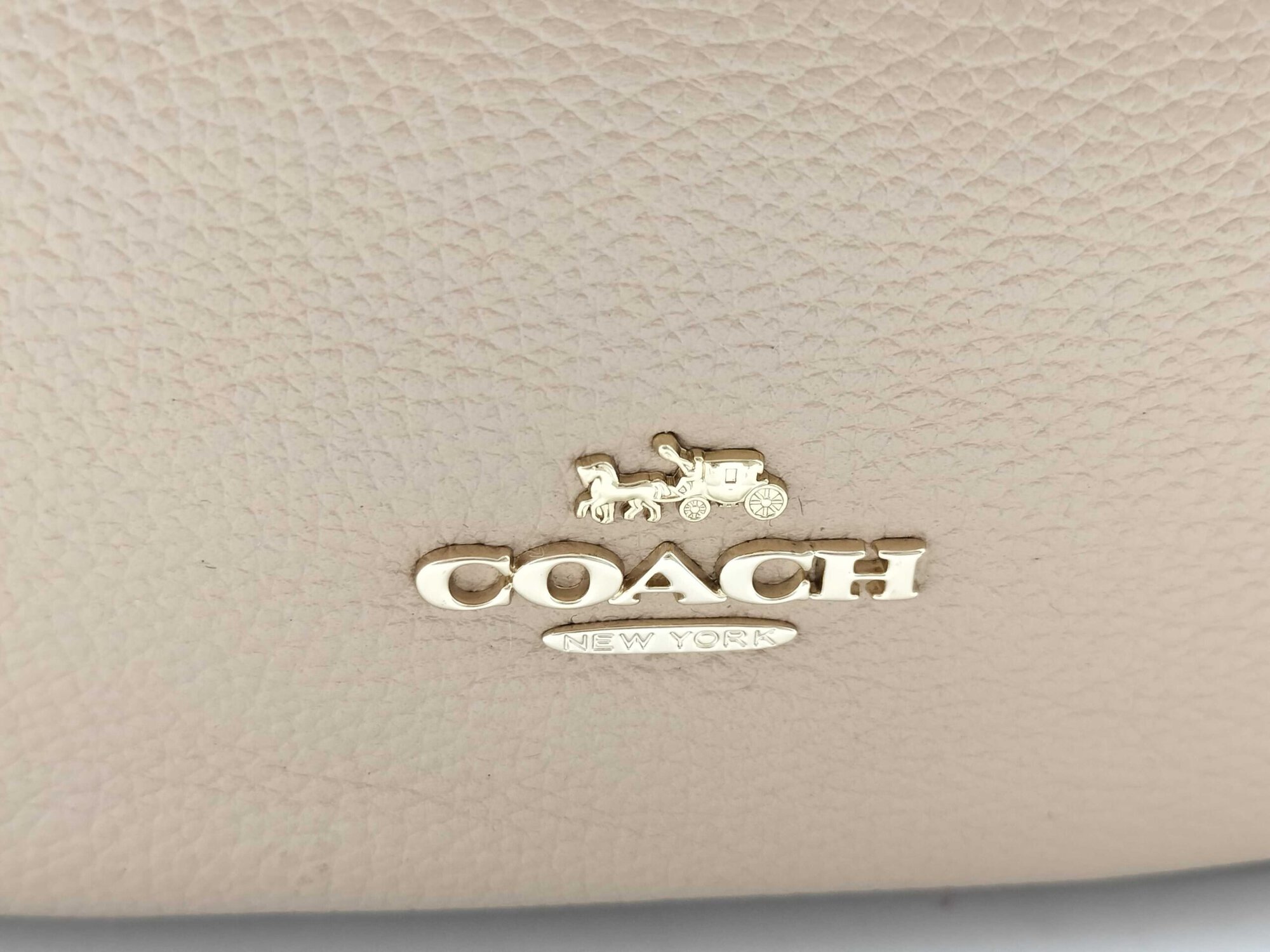 Close-up of gold-tone Coach Horse and Carriage metal logo on pebble leather