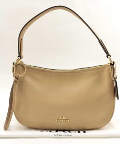 Front view of Coach Sutton pale gold metallic pebble leather shoulder bag resting on dust bag