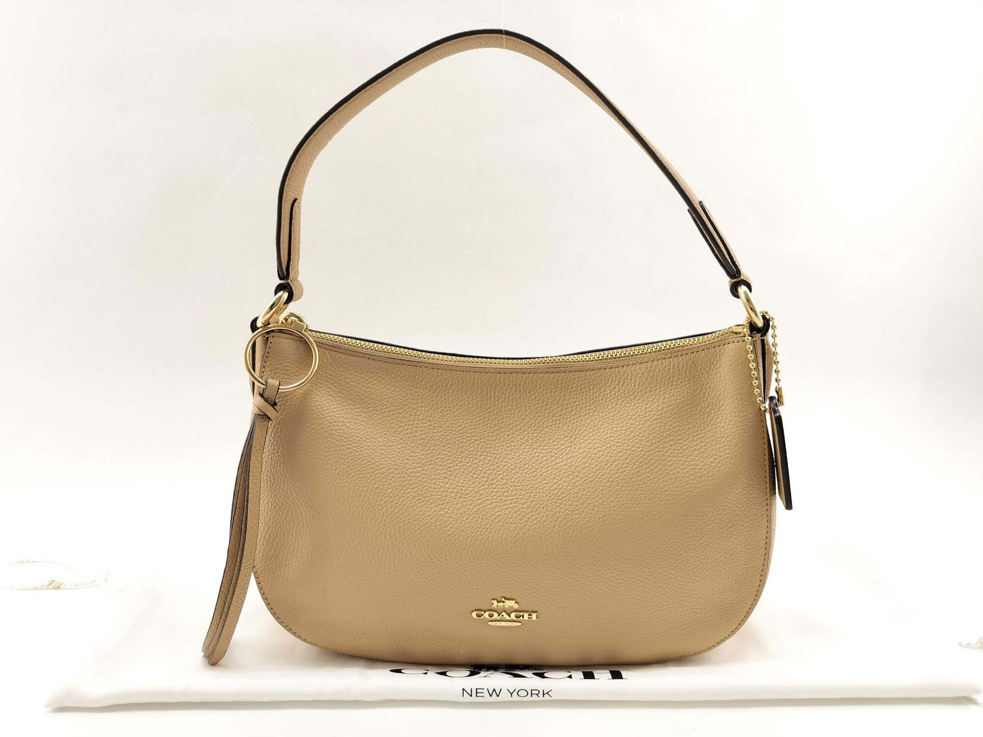 Front view of Coach Sutton pale gold metallic pebble leather shoulder bag resting on dust bag