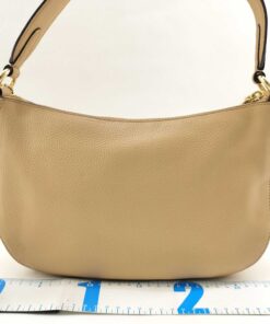 Back view of Coach Sutton pale gold shoulder bag against measuring tape showing width