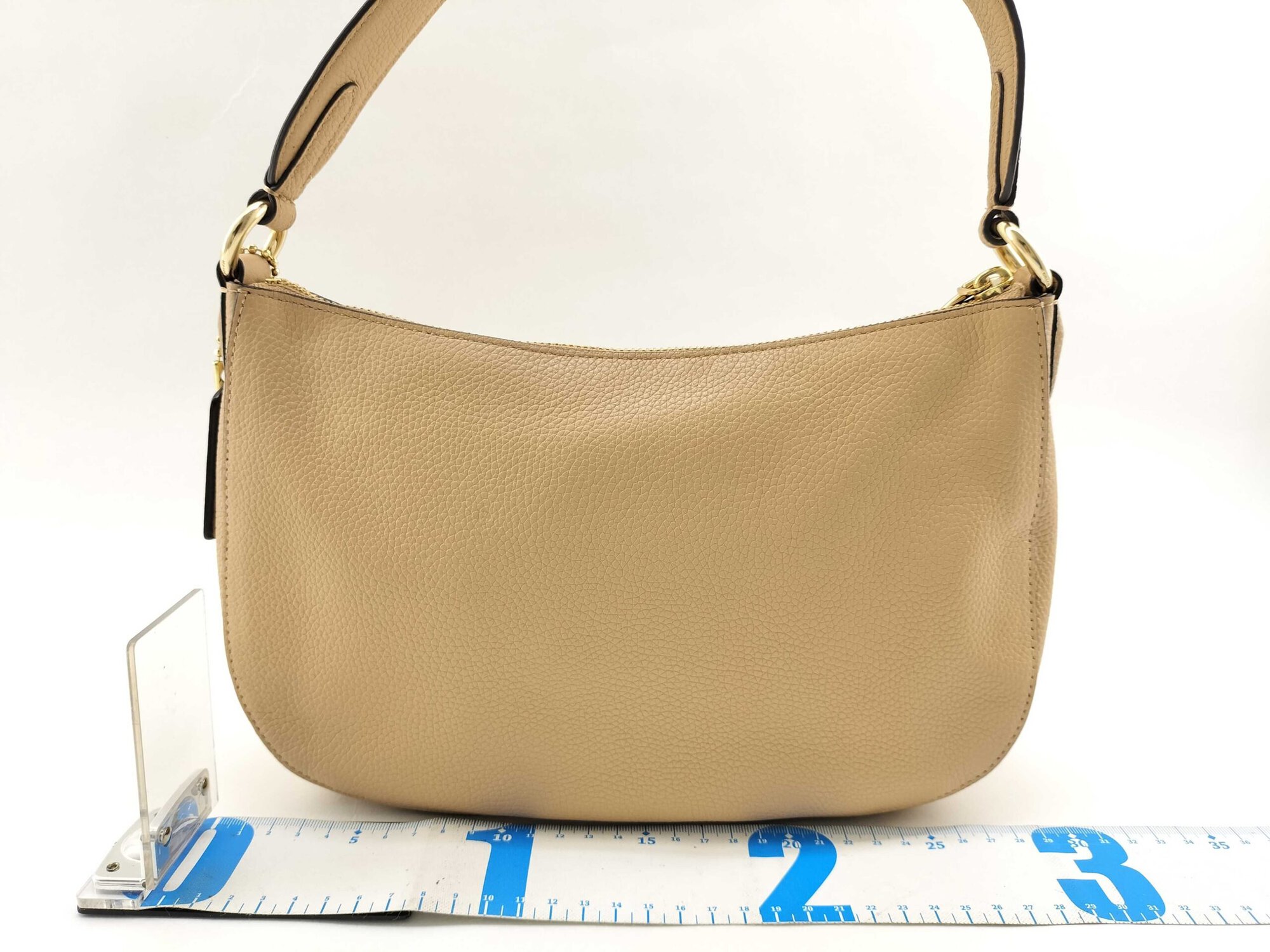 Back view of Coach Sutton pale gold shoulder bag against measuring tape showing width
