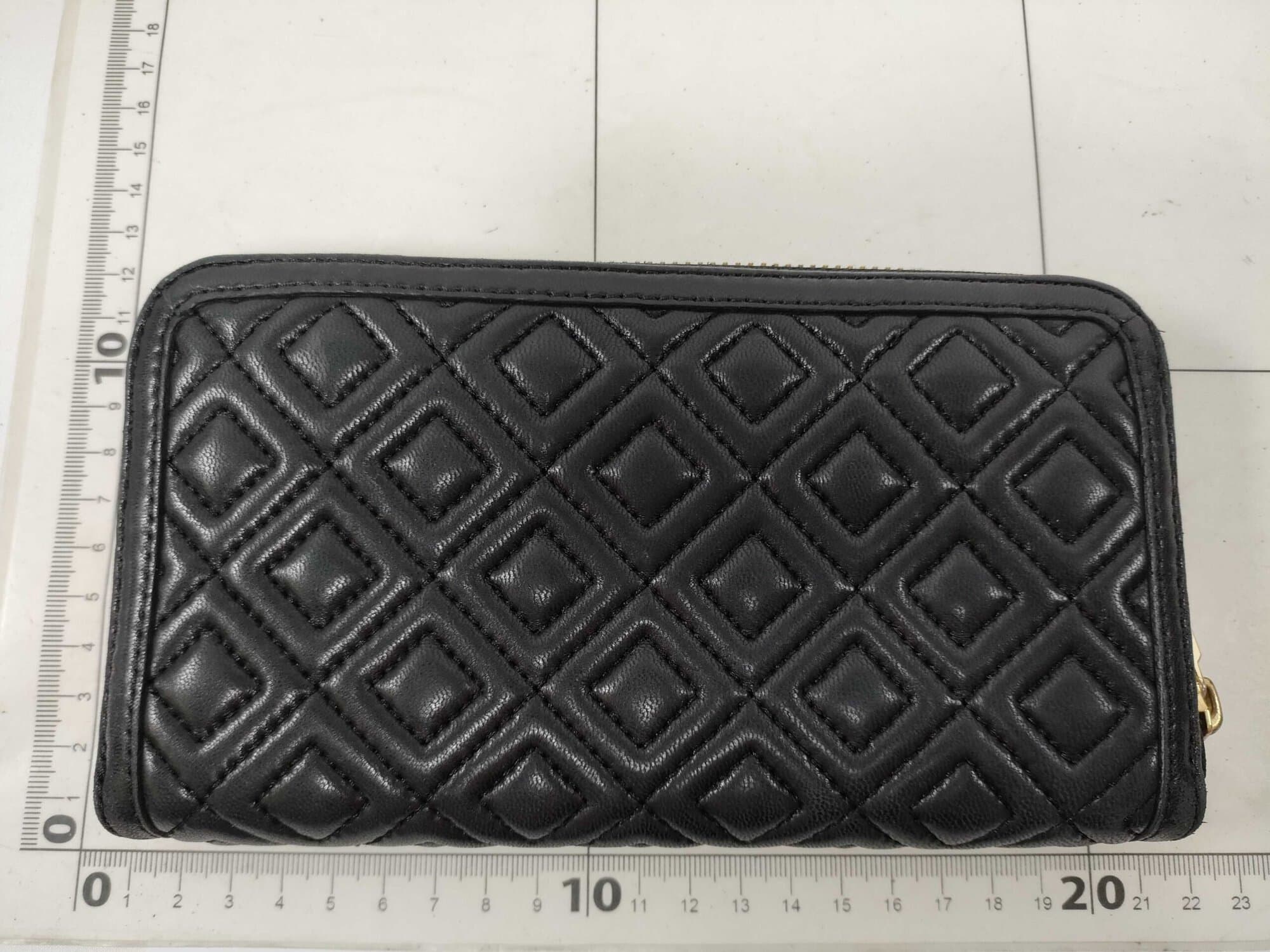 Back quilted panel of black Tory Burch Fleming continental wallet laid against a grid ruler.