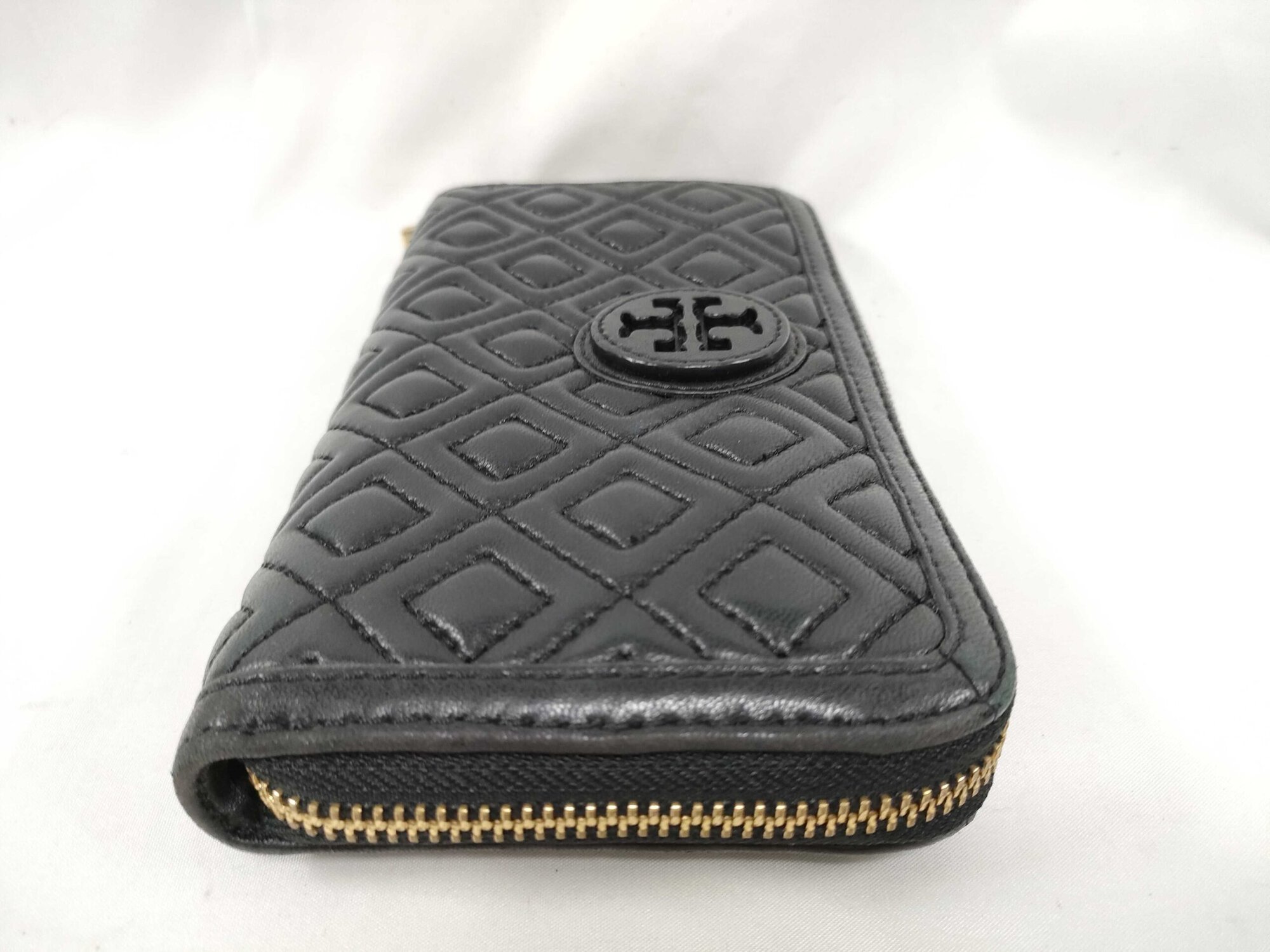 Side profile of black quilted leather Tory Burch wallet showing gusset fold and zipper end.
