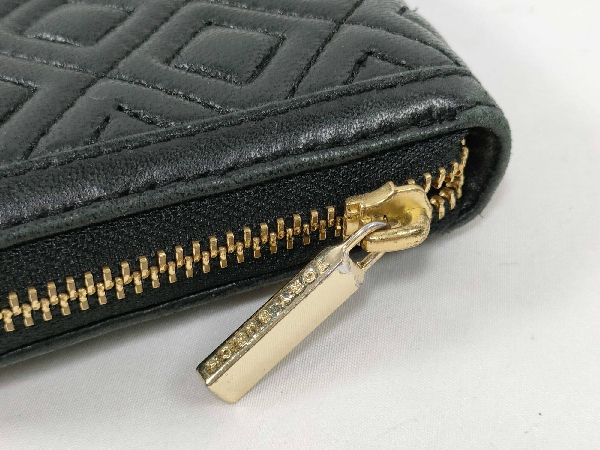 Close-up of gold-tone metal zipper pull engraved with Tory Burch logo lettering.