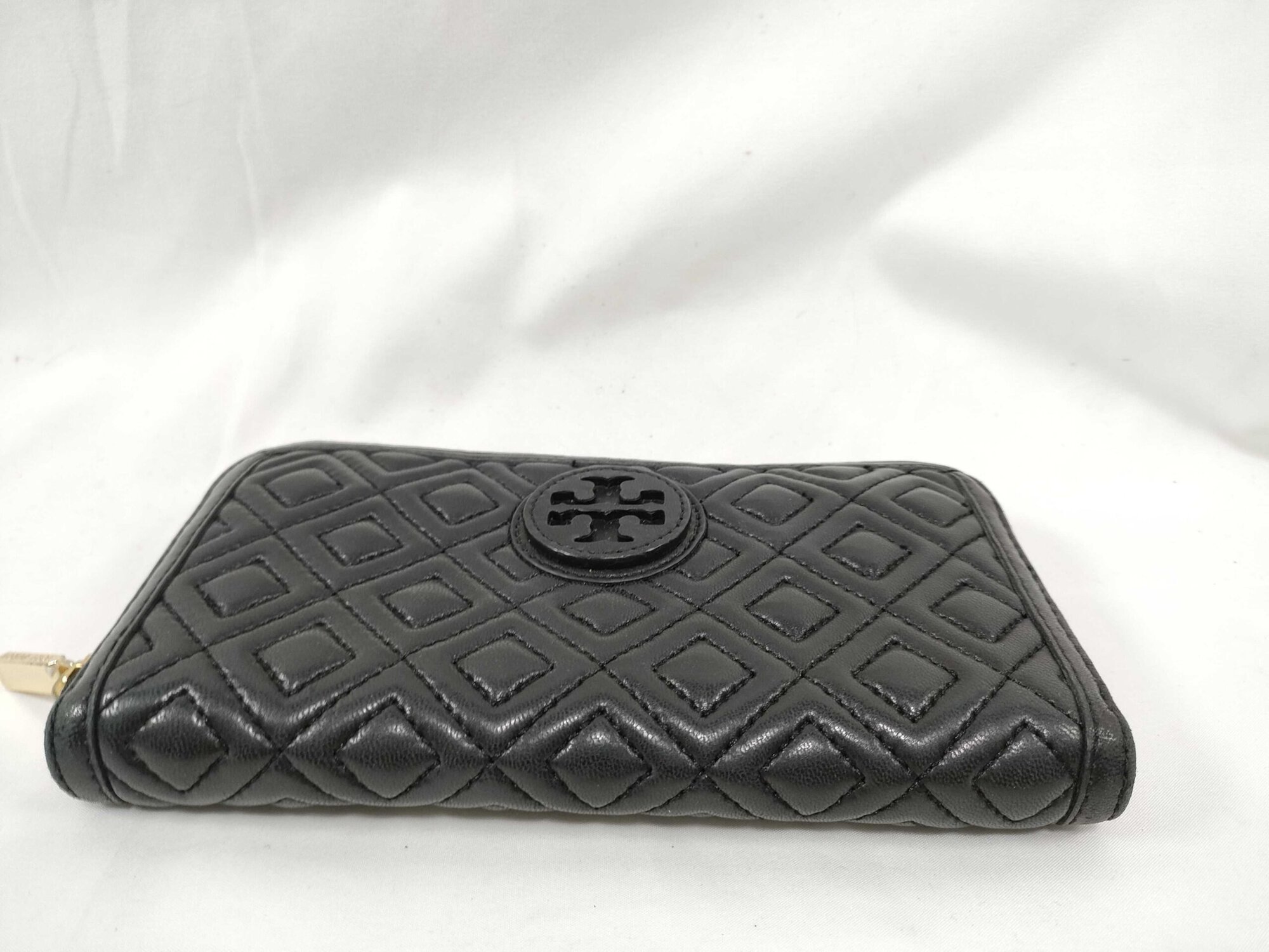 Bottom edge of black quilted leather Tory Burch continental wallet showing seam stitching.