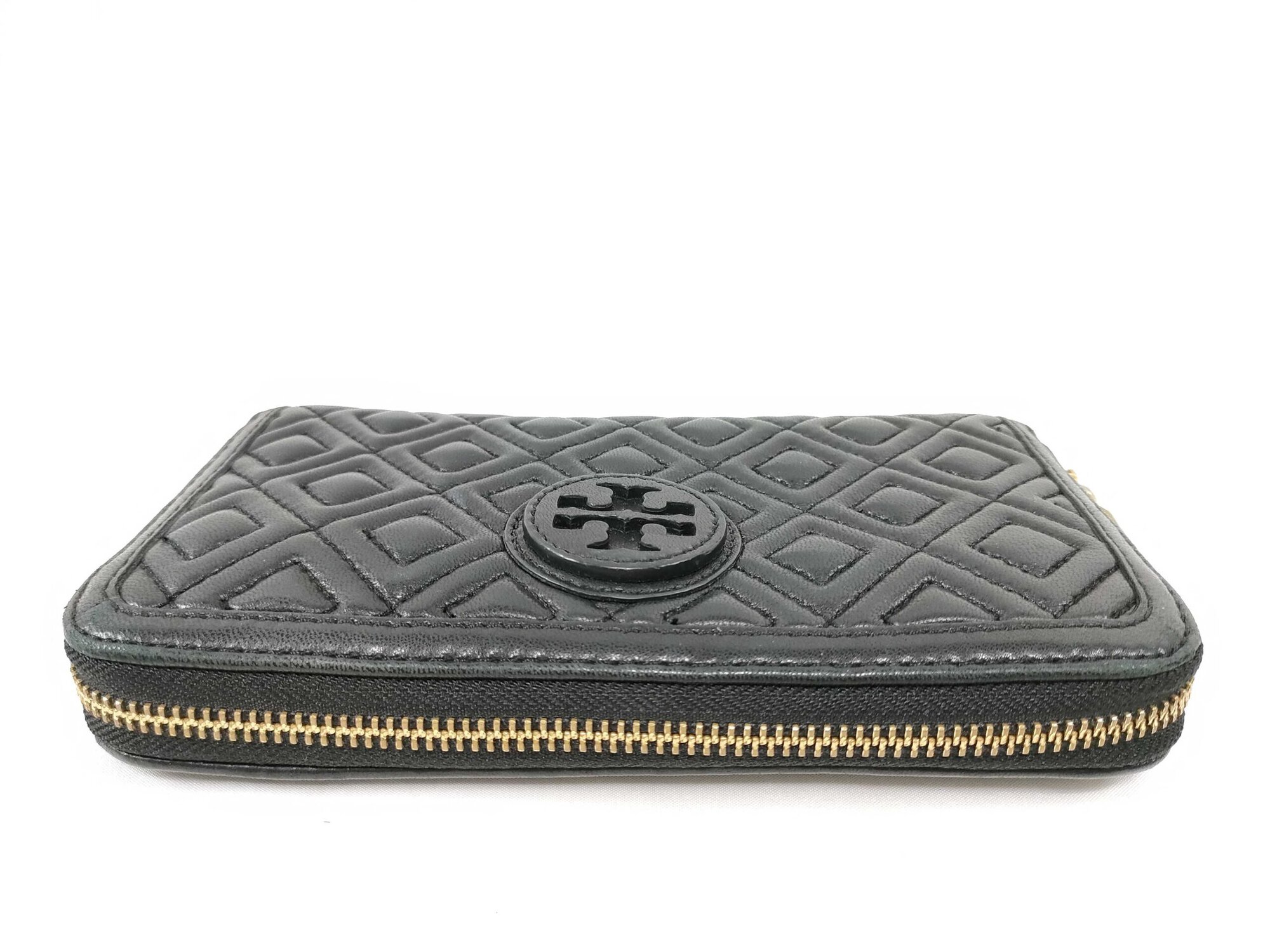 Top view of closed gold-tone zipper track along perimeter of black leather Tory Burch wallet.