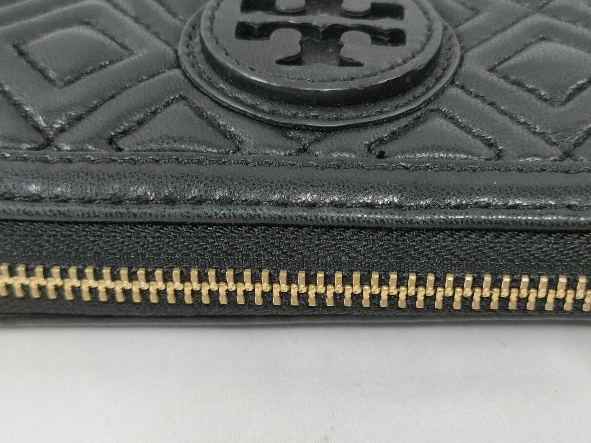 Detailed view of exterior stitched edge trim and gold-tone zipper teeth on black leather wallet.