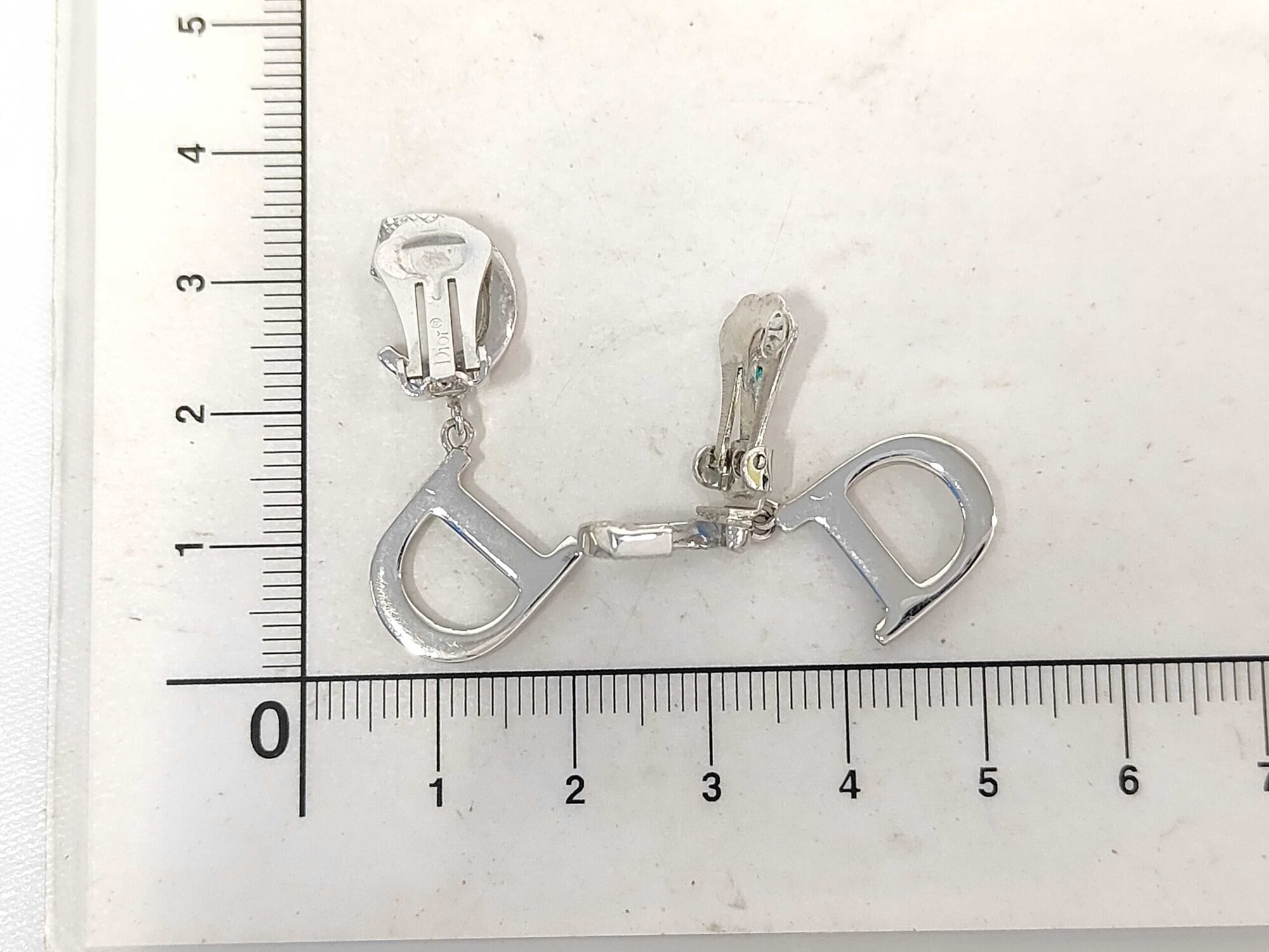 Christian Dior CD logo drop clip-on earrings positioned beside a metric centimeter ruler.