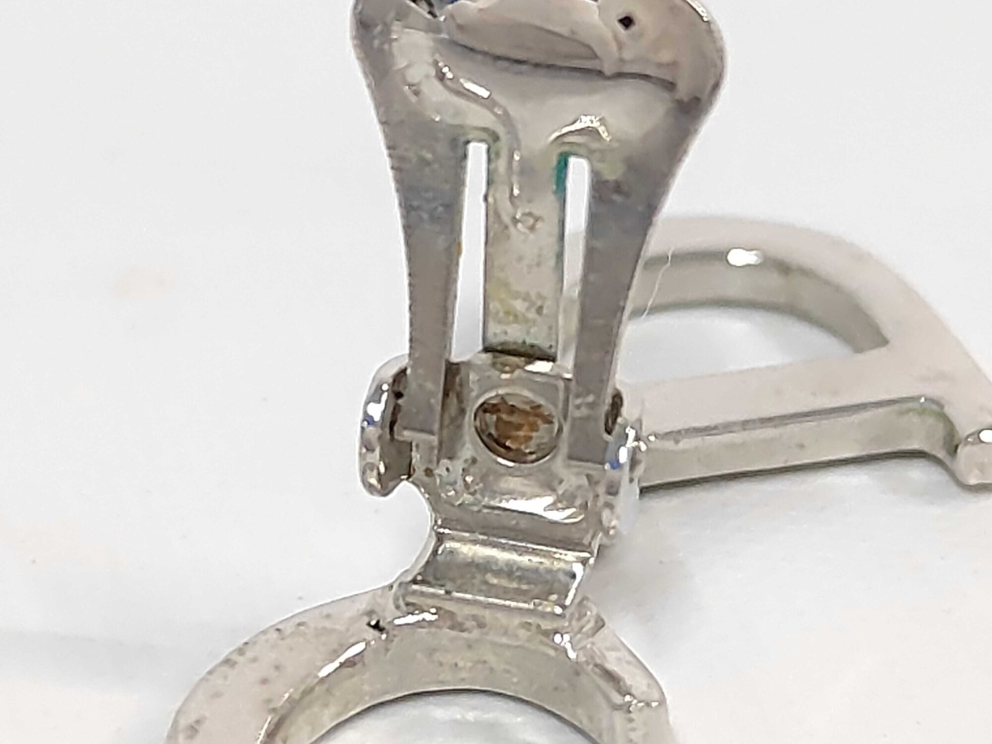 Macro view of earring clip-on hinge showing spring mechanism and localized tarnish.