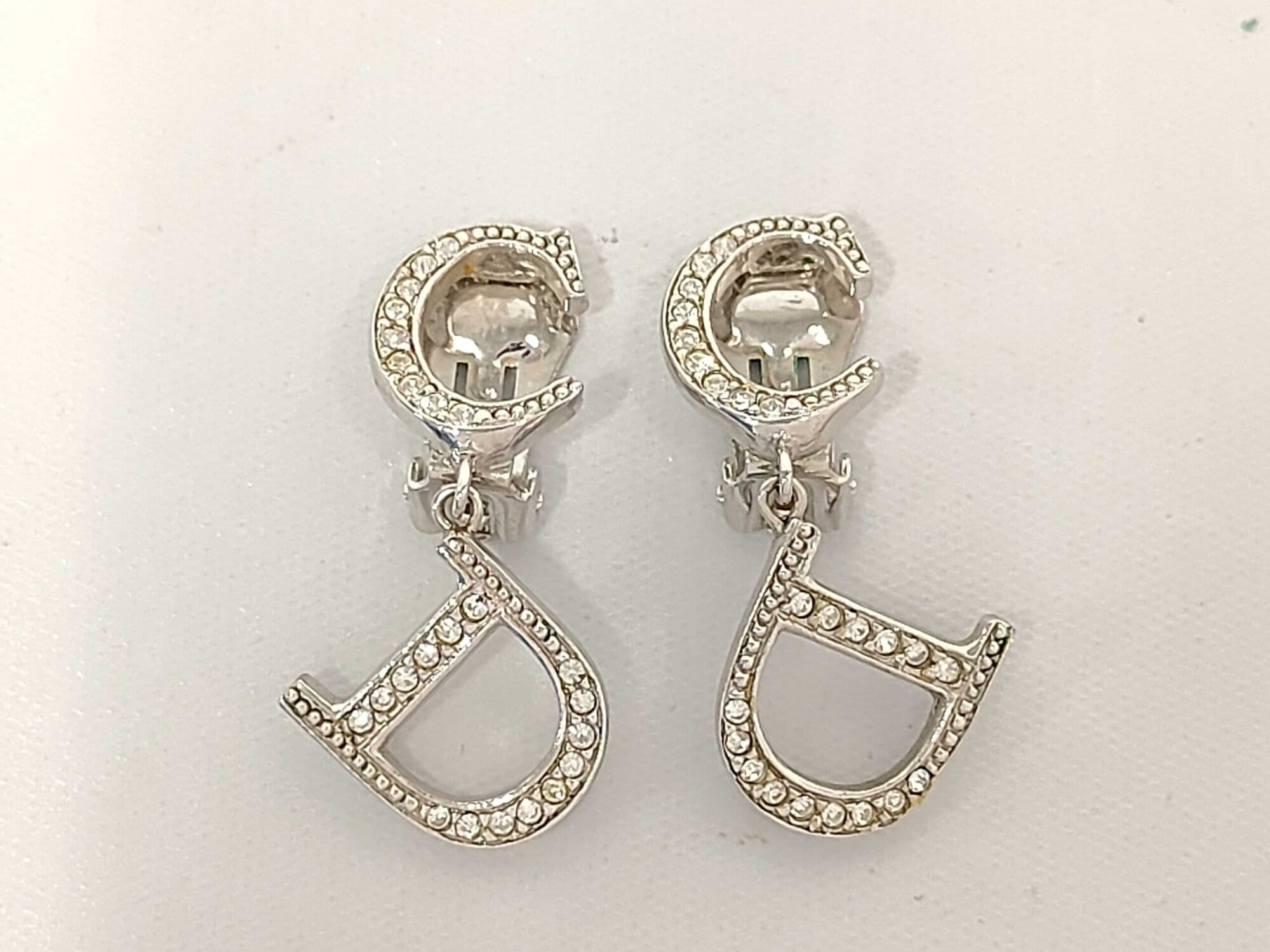 Front view of Christian Dior CD logo drop clip-on earrings in silver-tone metal with clear accents.