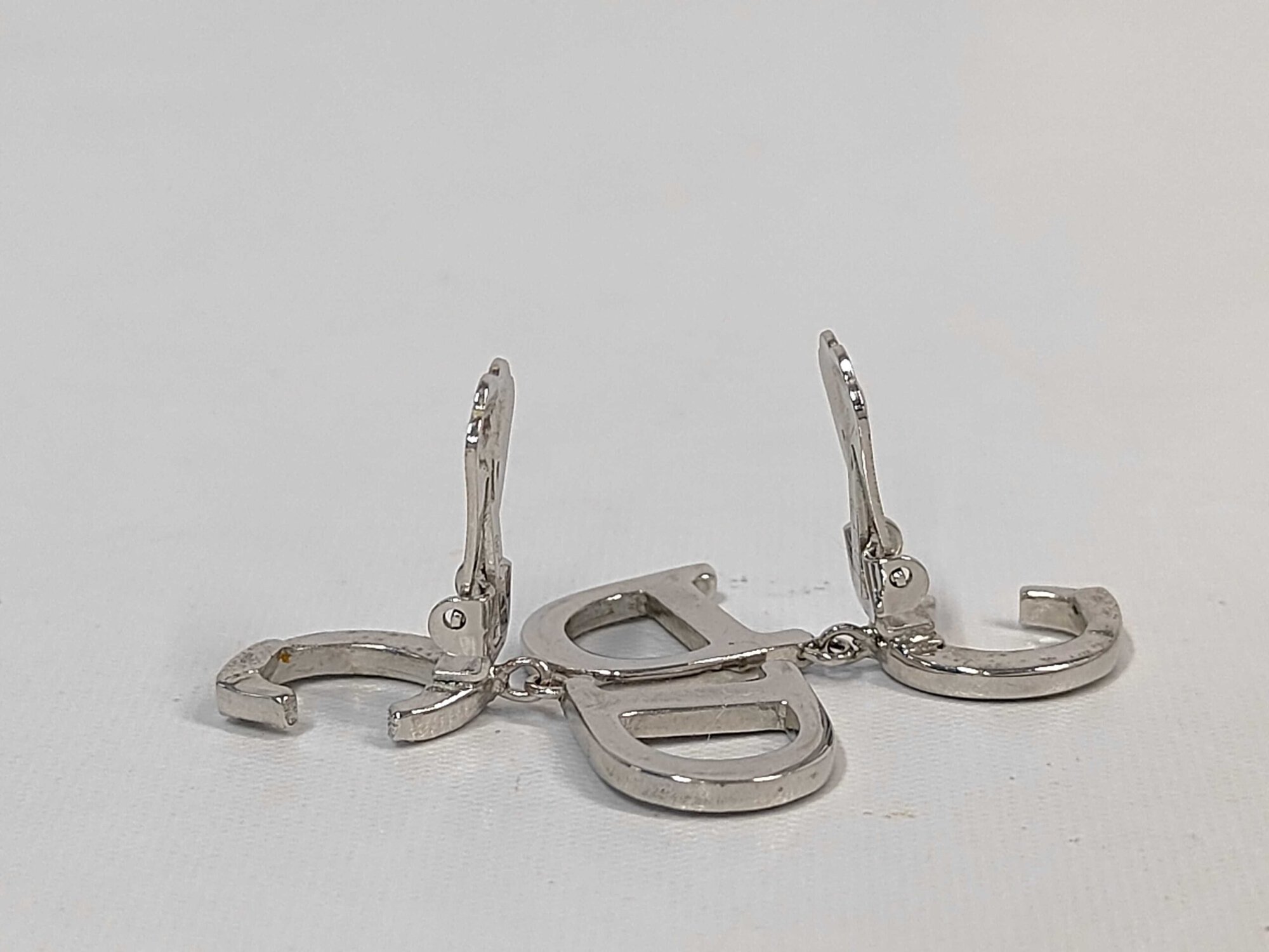 Side angle view of Christian Dior CD logo drop earrings resting with paddle clips upright.