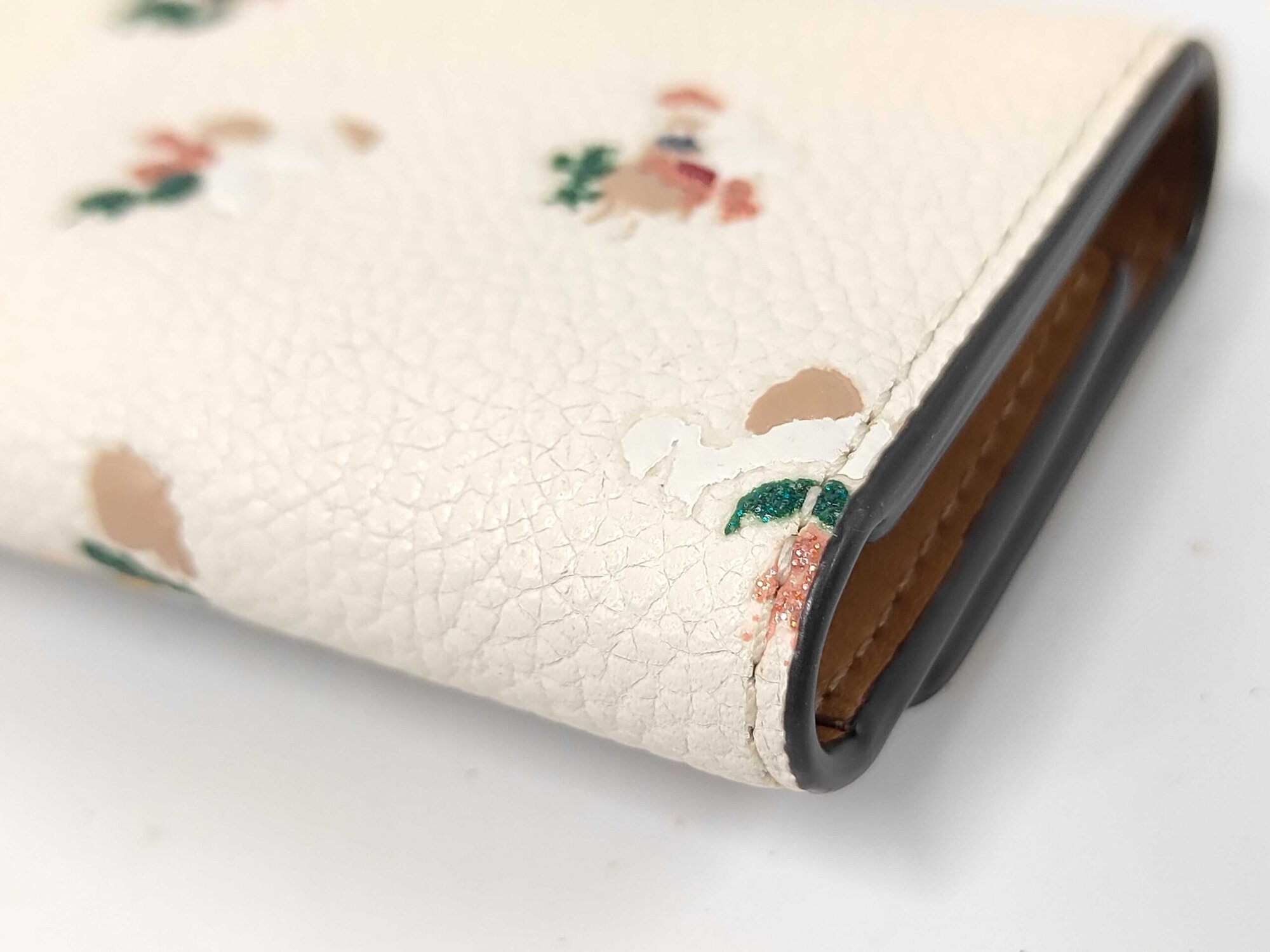 Close-up of lower corner edge showing slight rubbing on Coach floral key case.