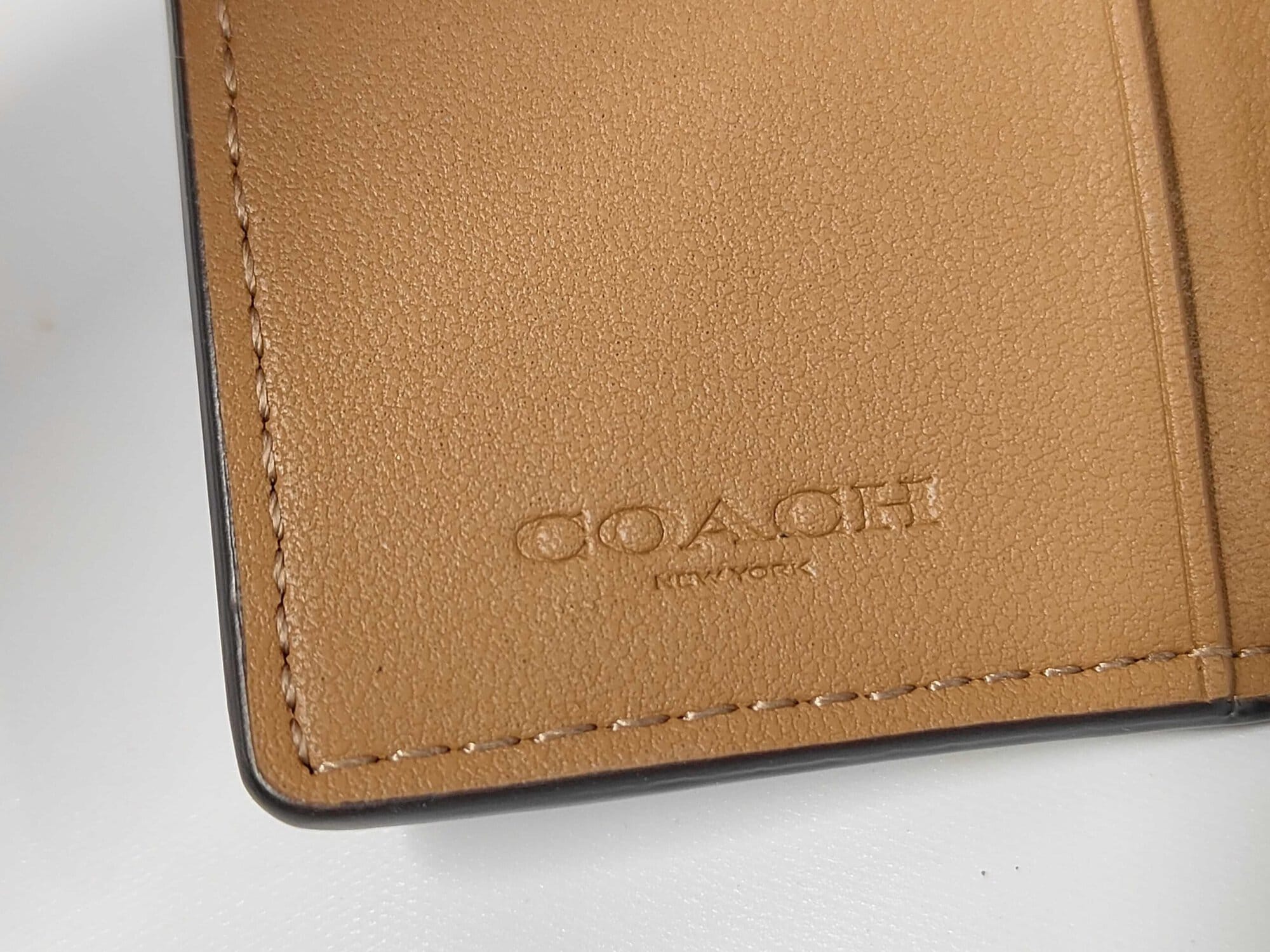 Close-up of debossed Coach New York logo on tan leather interior.