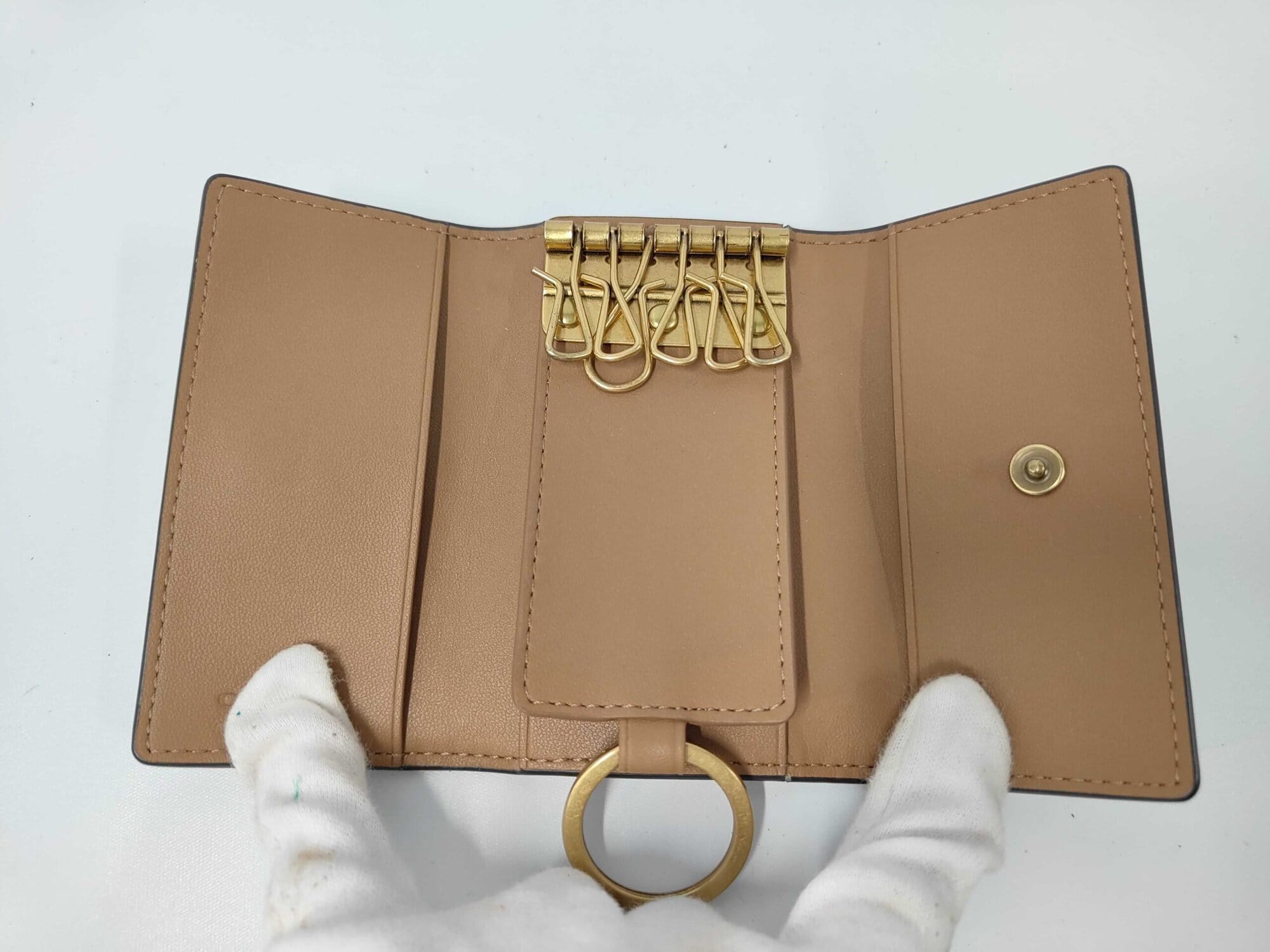 Open interior view of Coach key case showing tan leather, six key hooks, and key ring.