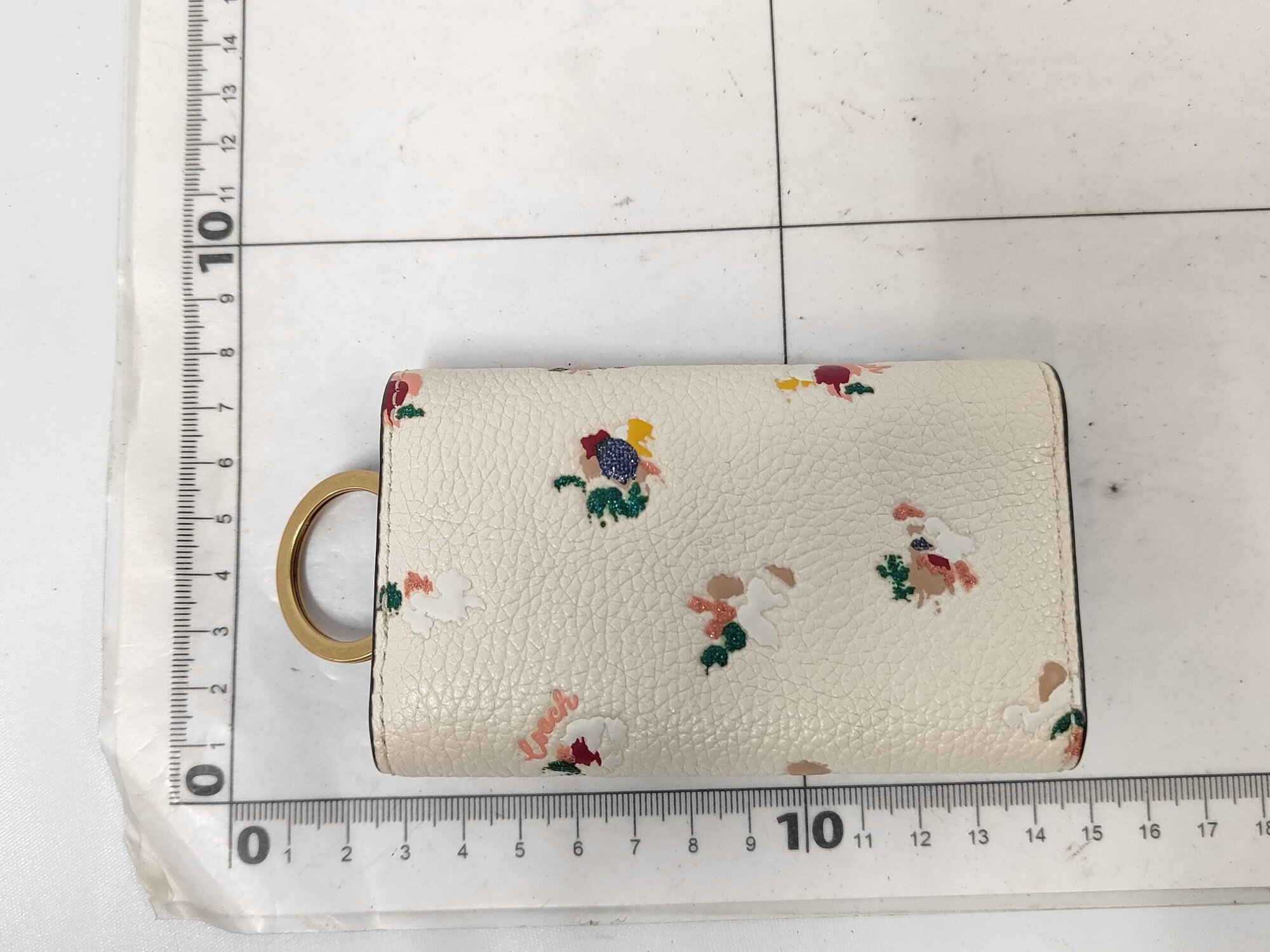 Back view of Coach floral key case positioned on a metric measuring grid.