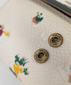 Close-up of dual Coach engraved snap studs on front pebble leather panel.