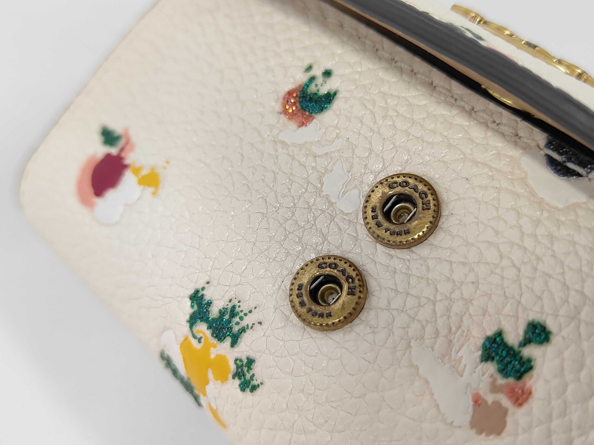Close-up of dual Coach engraved snap studs on front pebble leather panel.