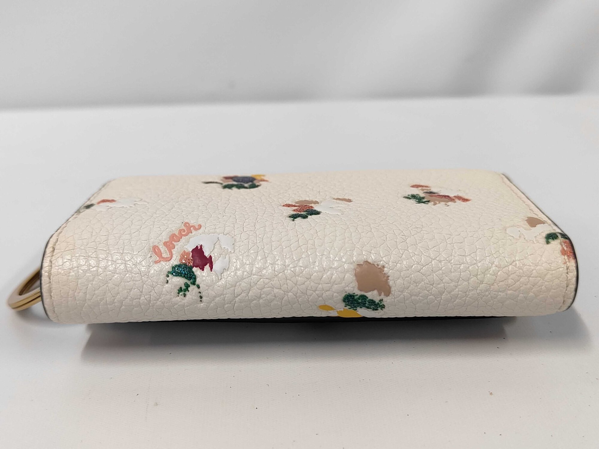 Bottom spine view of folded Coach chalk pebble leather floral key case.