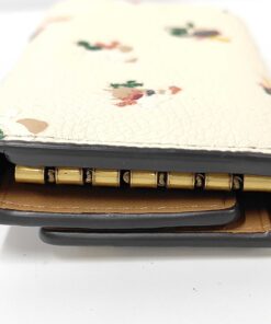 Side profile of folded Coach key case showing black edge glazing and interior hardware.