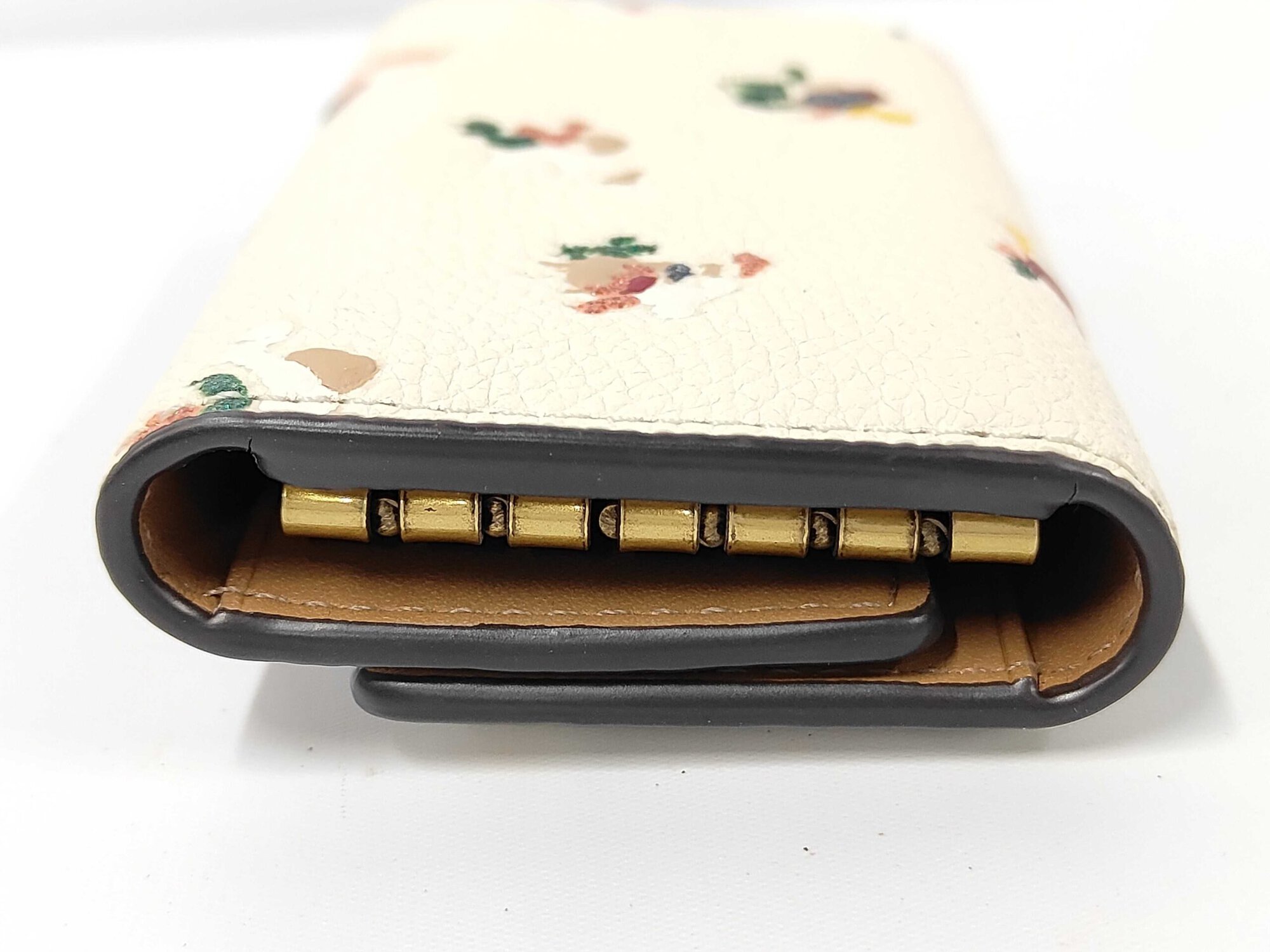 Side profile of folded Coach key case showing black edge glazing and interior hardware.