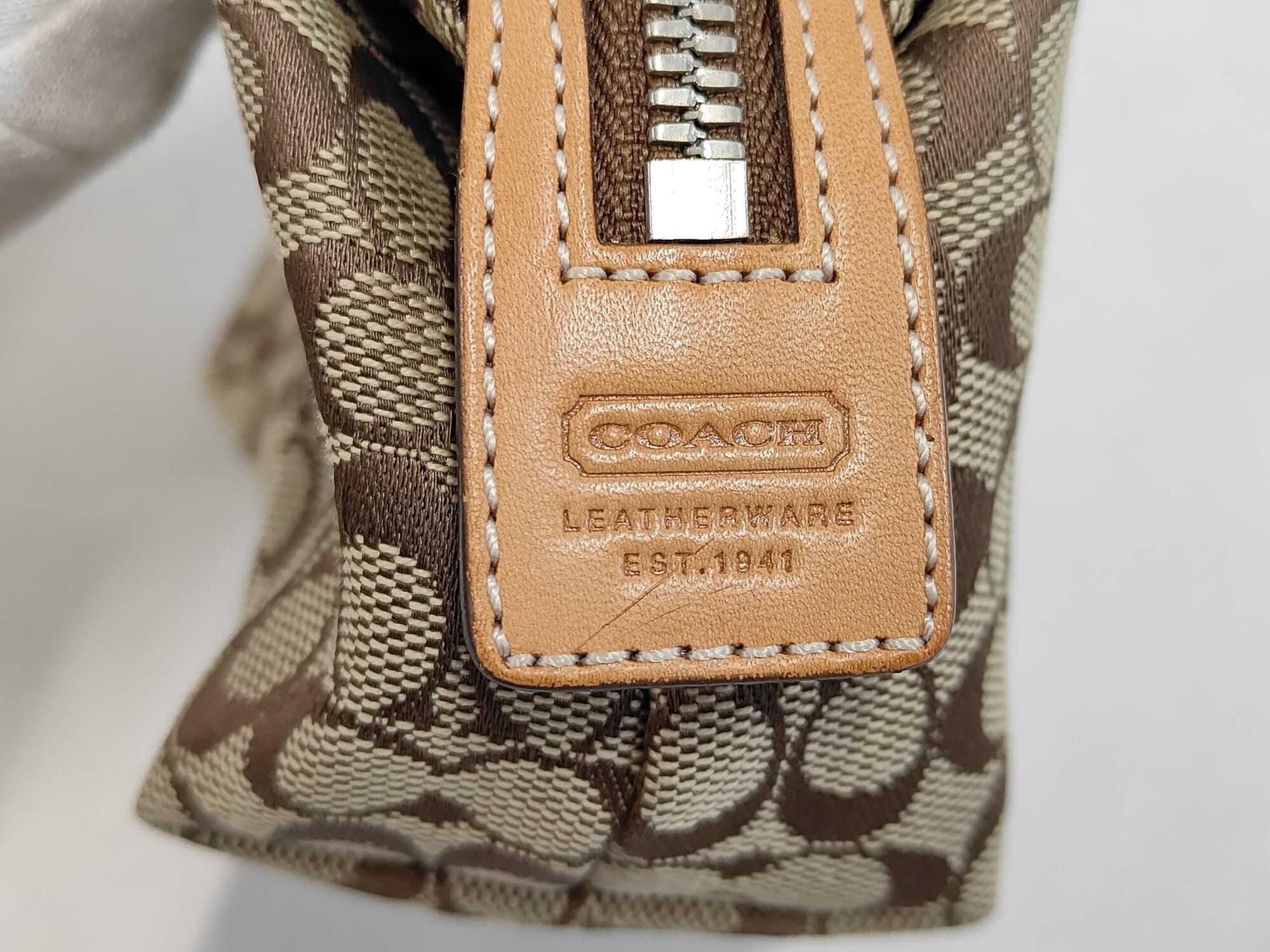 Close-up of debossed Coach leather side trim tab and zipper end