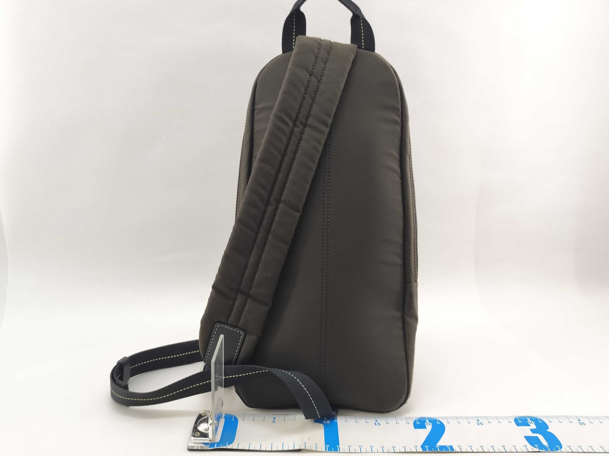 Rear view of Coach sling pack showing padded mesh shoulder strap and base width ruler.