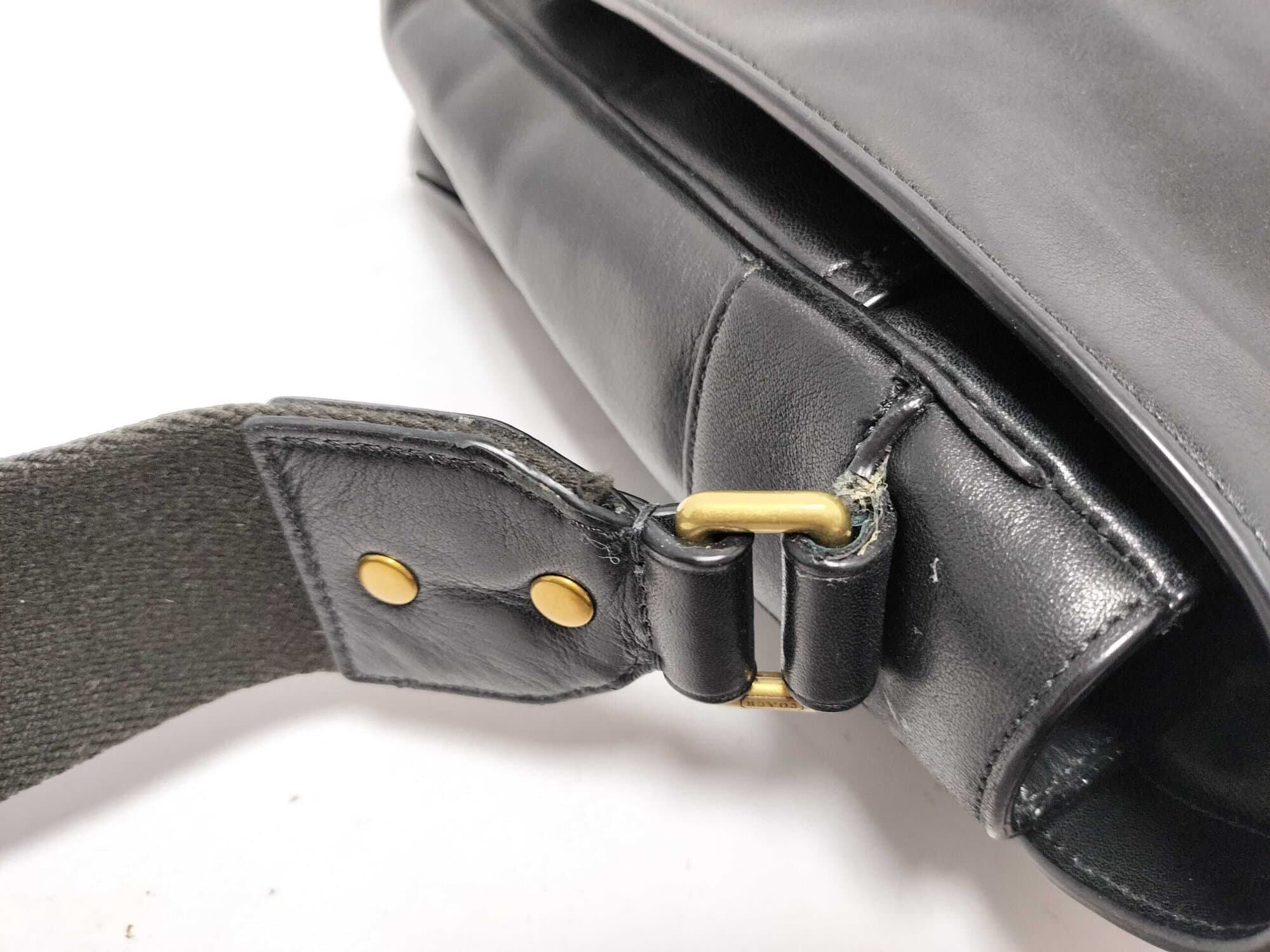 Close-up of leather strap anchor tab and brass-tone connector ring.