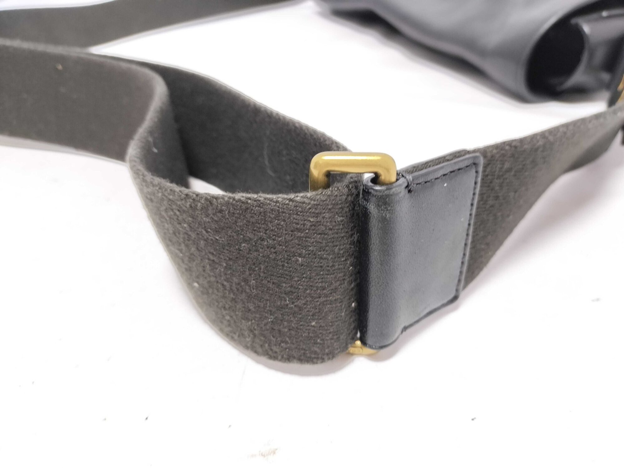 Close-up of brass-tone metal slider buckle on webbed strap.