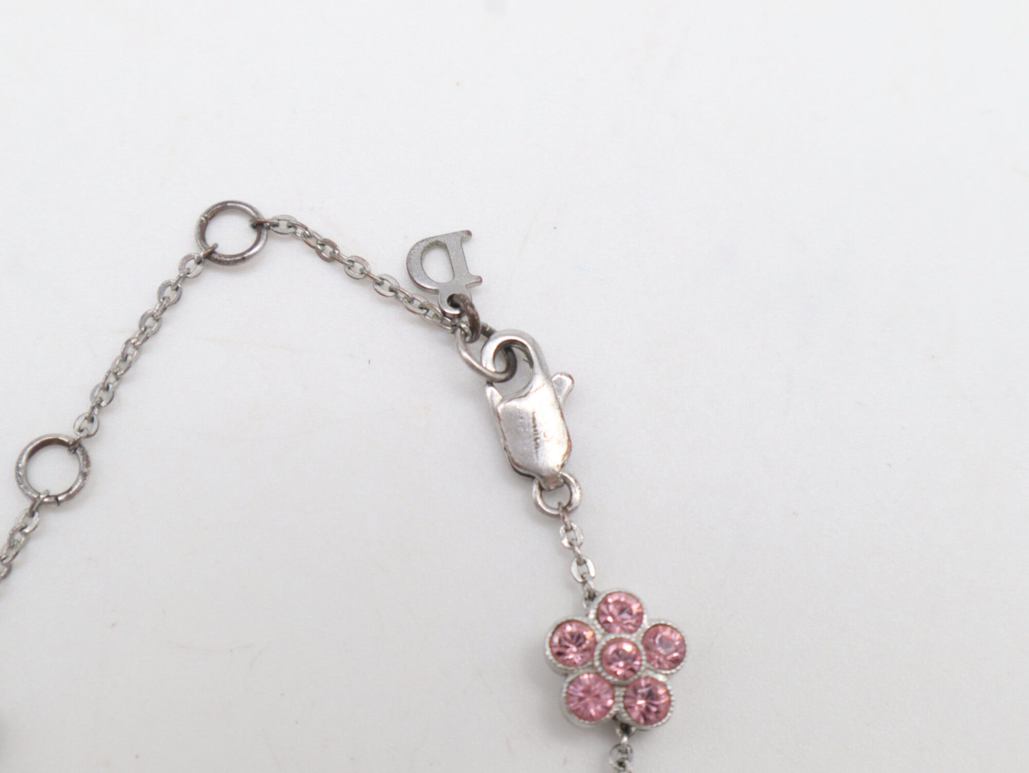 Close-up of the lobster claw clasp, Dior logo charm, and adjacent pink floral charm on chain.