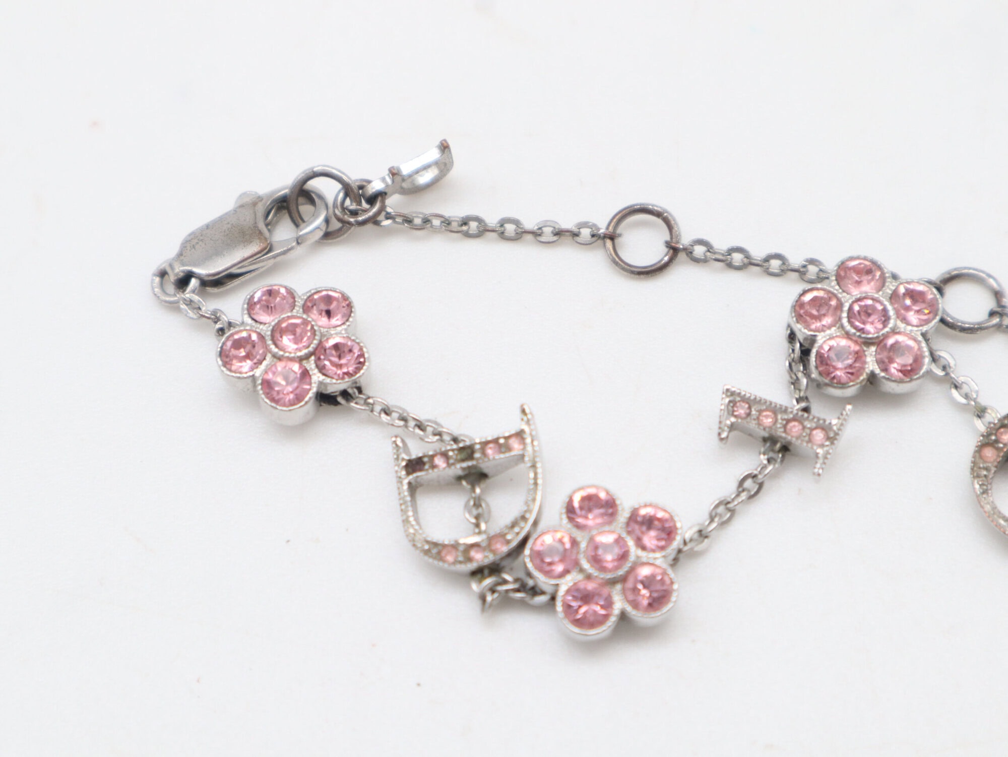 Macro view of the pink stone-set flower charms alongside the D and I letter charms on the silver-tone chain.