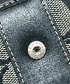 Close-up of engraved silver-tone Coach snap button on black leather stripe.