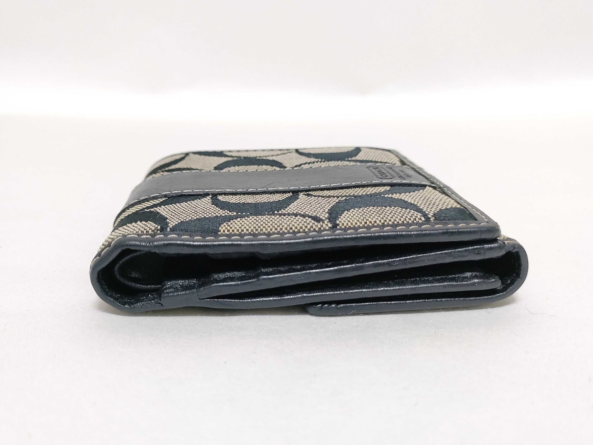 Side edge view of folded Coach bifold wallet showing thickness and layered construction.