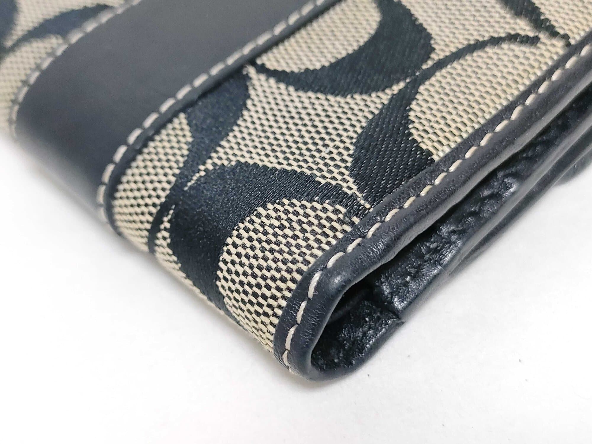 Close-up of corner edge binding and contrast white stitching on Coach bifold wallet.