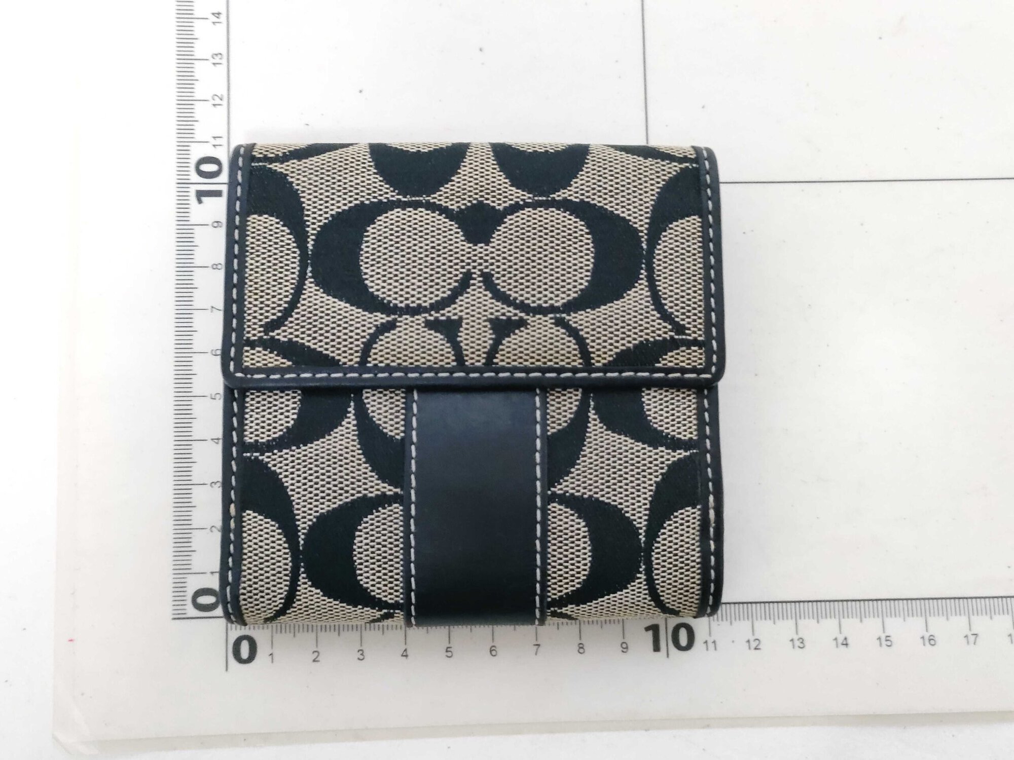 Back flap view of Coach compact bifold wallet positioned on a centimeter measuring grid.