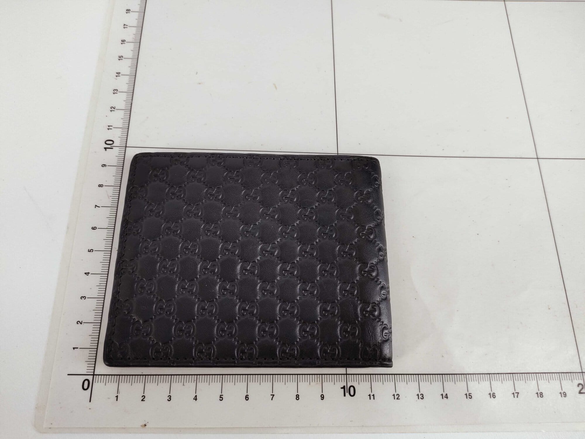 Gucci black leather bifold wallet displayed flat on a metric measuring grid